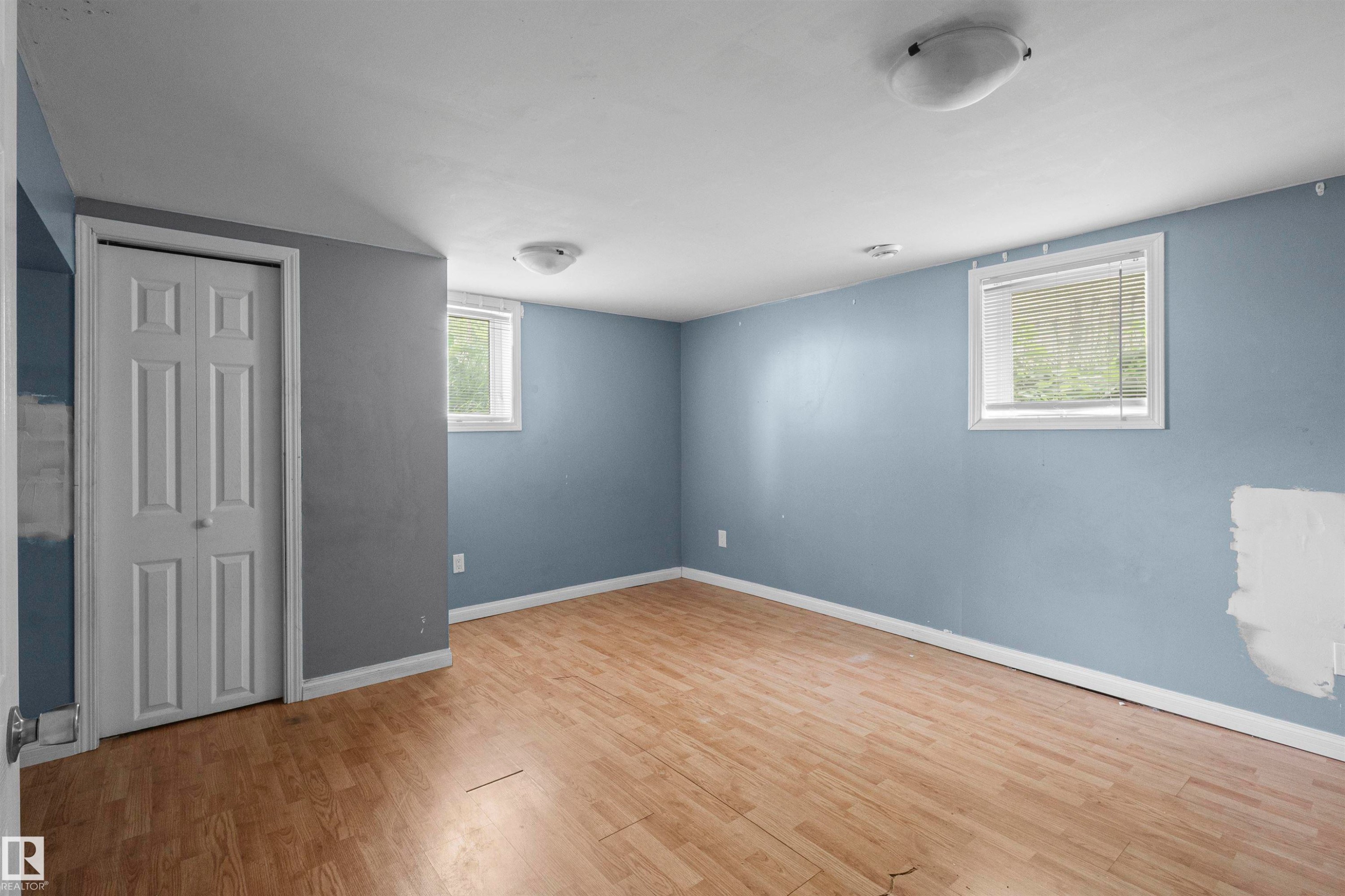 Spacious room featuring wood-finish flooring, light blue walls, and two windows with white blinds - 7520 106 Street, Edmonton, AB