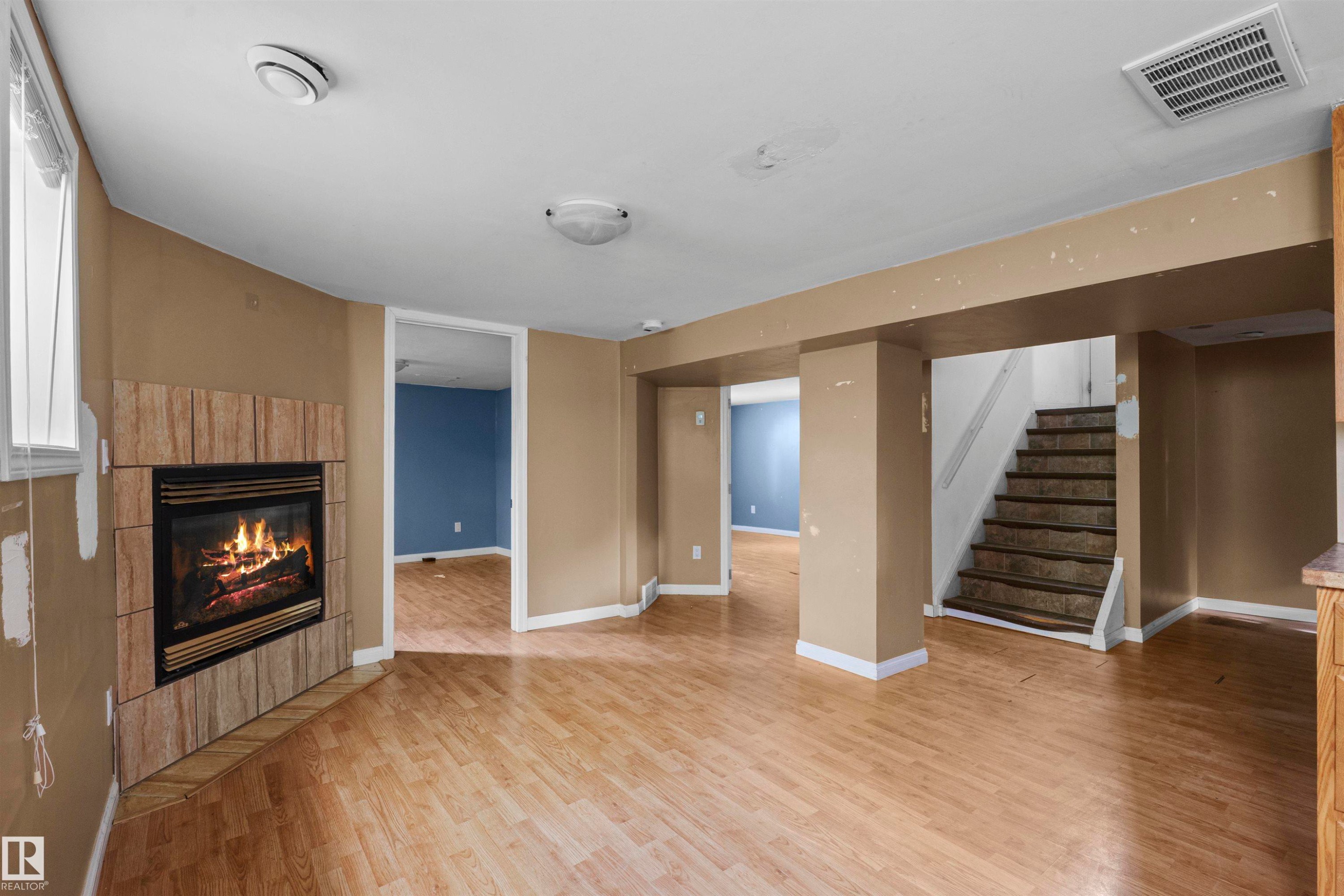 Living area featuring wood-finish flooring, a corner fireplace with a tiled surround, and recessed ceiling lighting - 7520 106 Street, Edmonton, AB