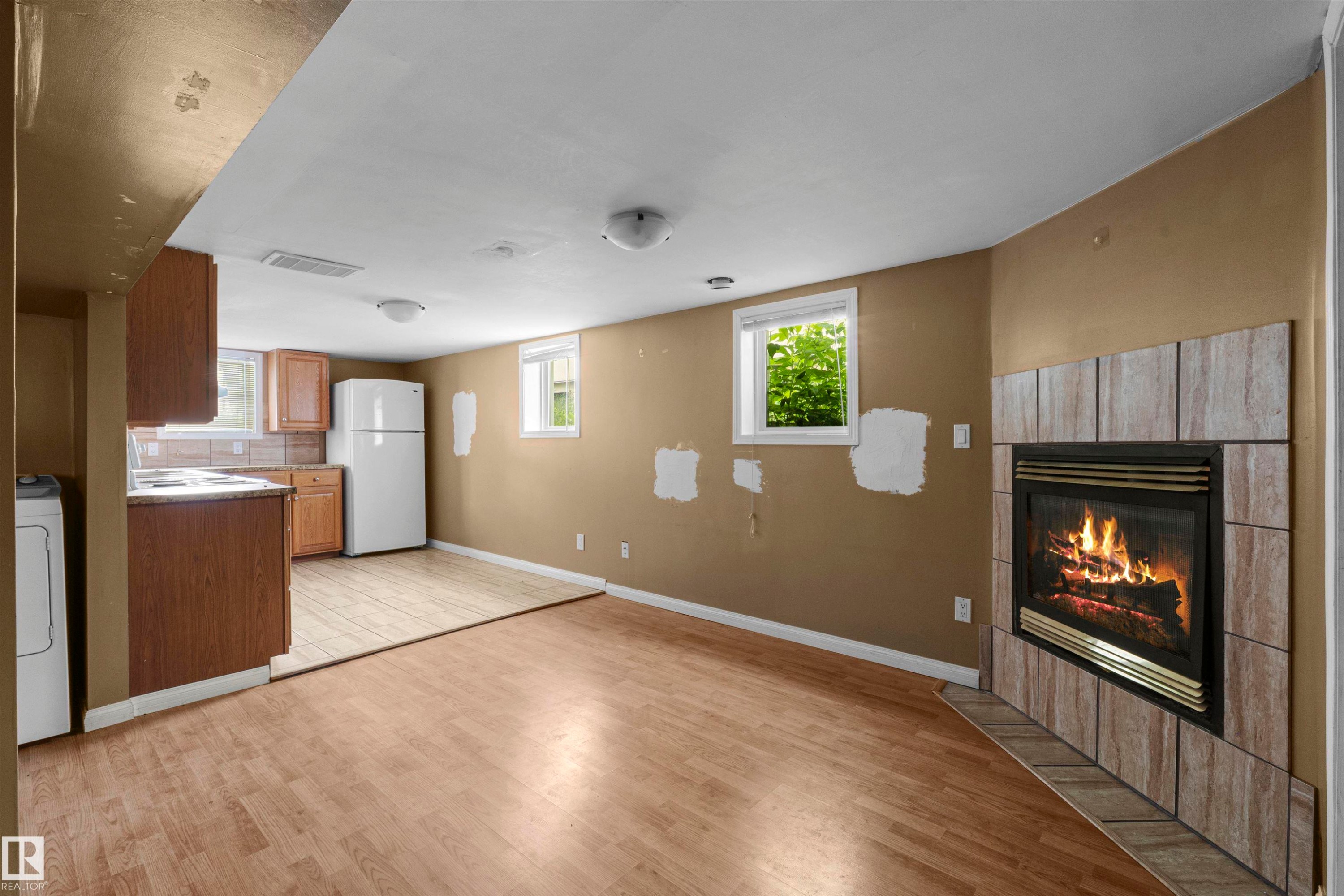 Spacious room featuring wood-finish flooring, a tile-surround fireplace, and two windows - 7520 106 Street, Edmonton, AB