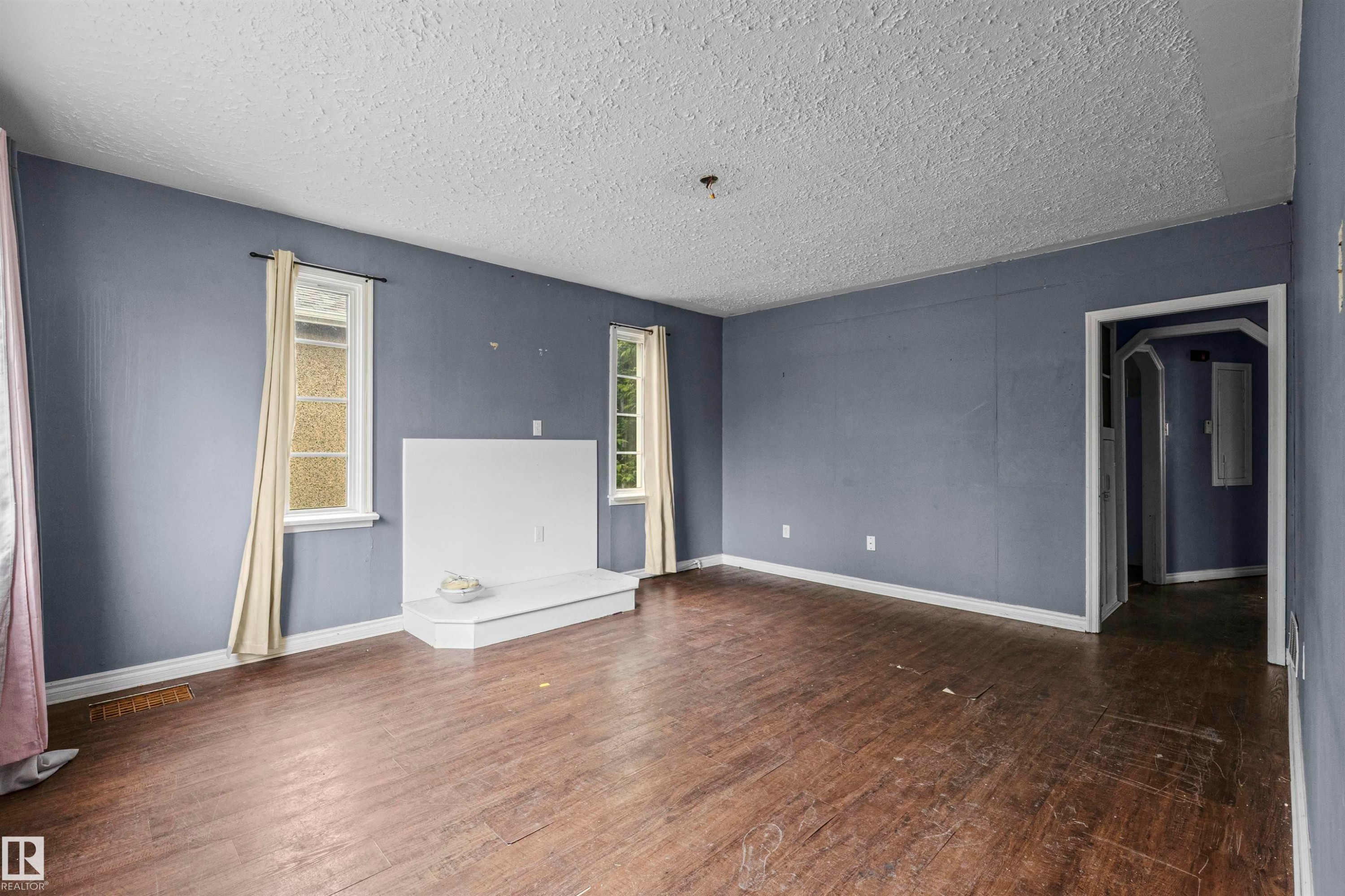 Spacious room featuring wood-finish flooring, light blue walls, and a textured white ceiling - 7520 106 Street, Edmonton, AB