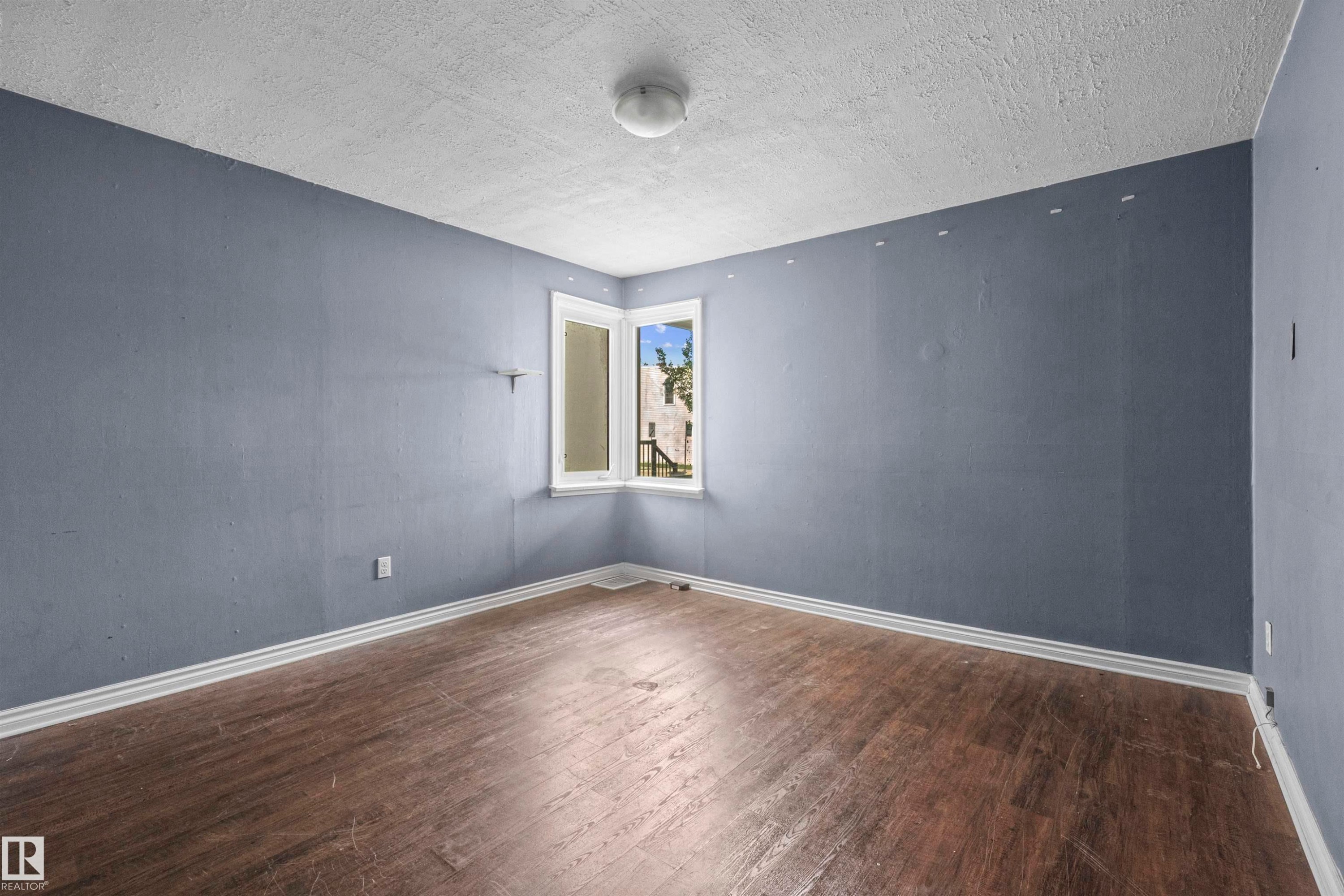 Room featuring wood-finish flooring, white baseboards, and a corner window with white trim - 7520 106 Street, Edmonton, AB