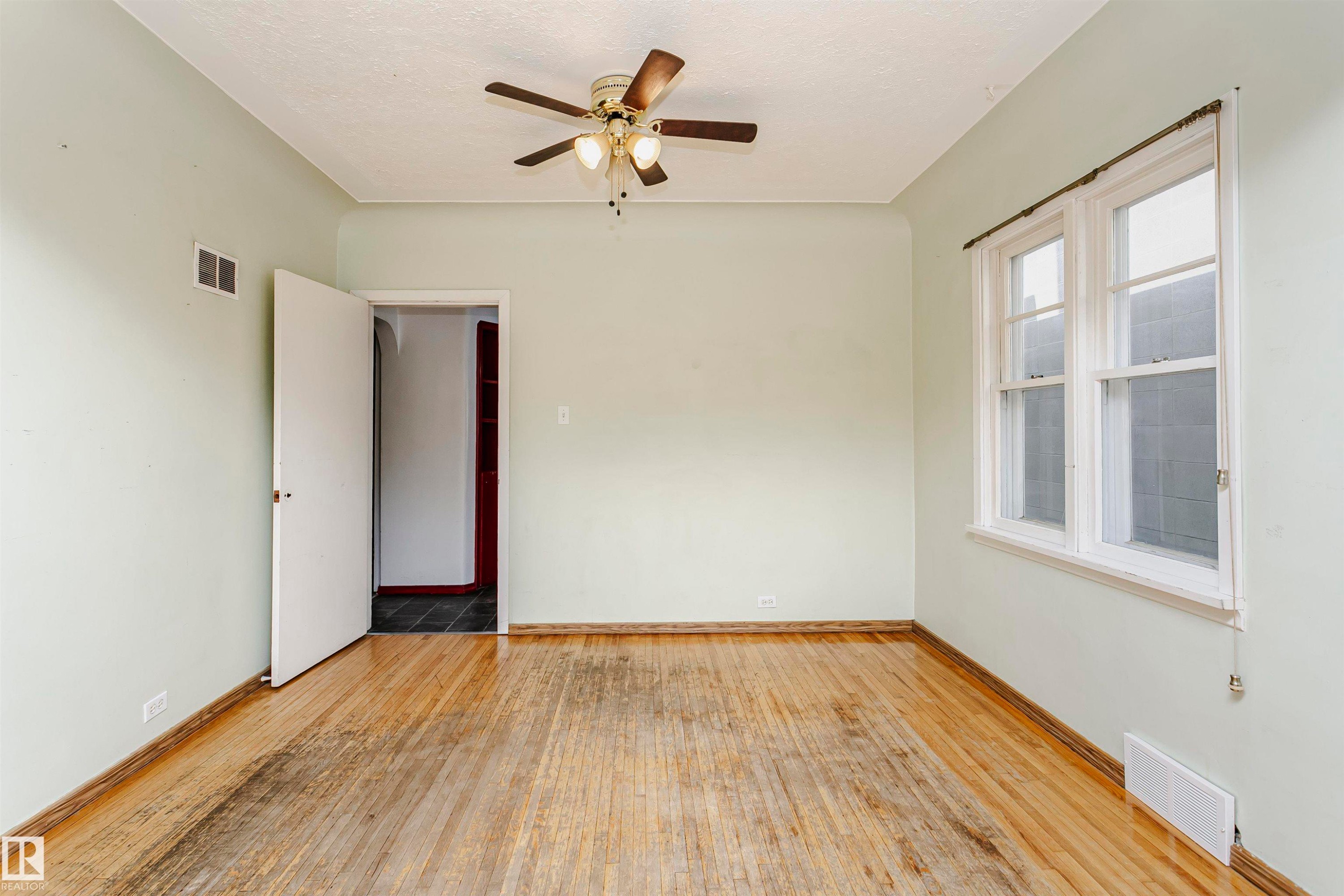 Spacious room featuring wood-finish flooring, light-colored walls, a ceiling fan, and white-framed windows - 10035 81 Avenue Nw, Edmonton, AB - Indoor Photo Showing Other Room