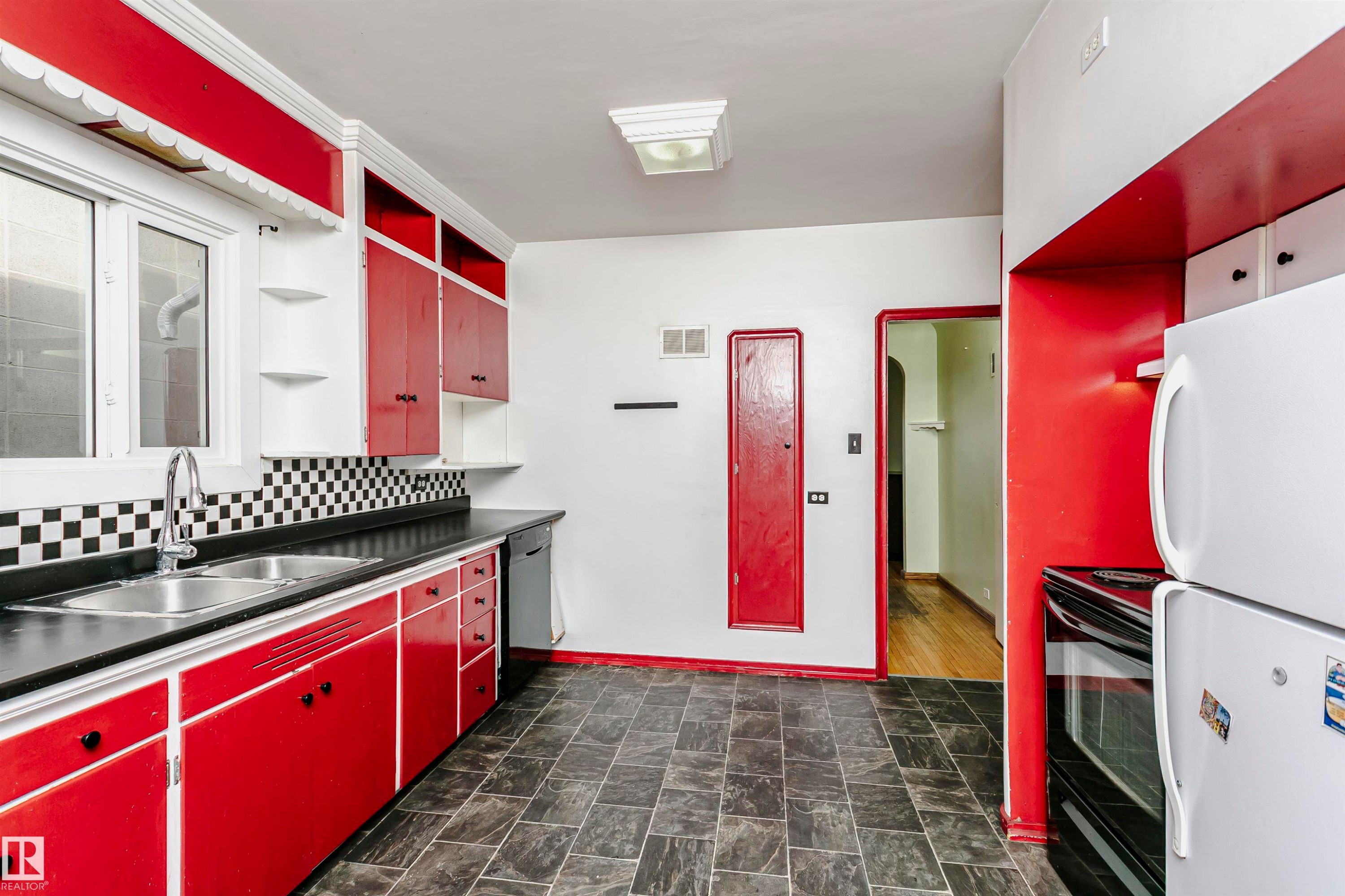 Kitchen featuring red cabinetry, black countertops, and a checkerboard backsplash - 10035 81 Avenue Nw, Edmonton, AB - Indoor Photo Showing Kitchen With Double Sink