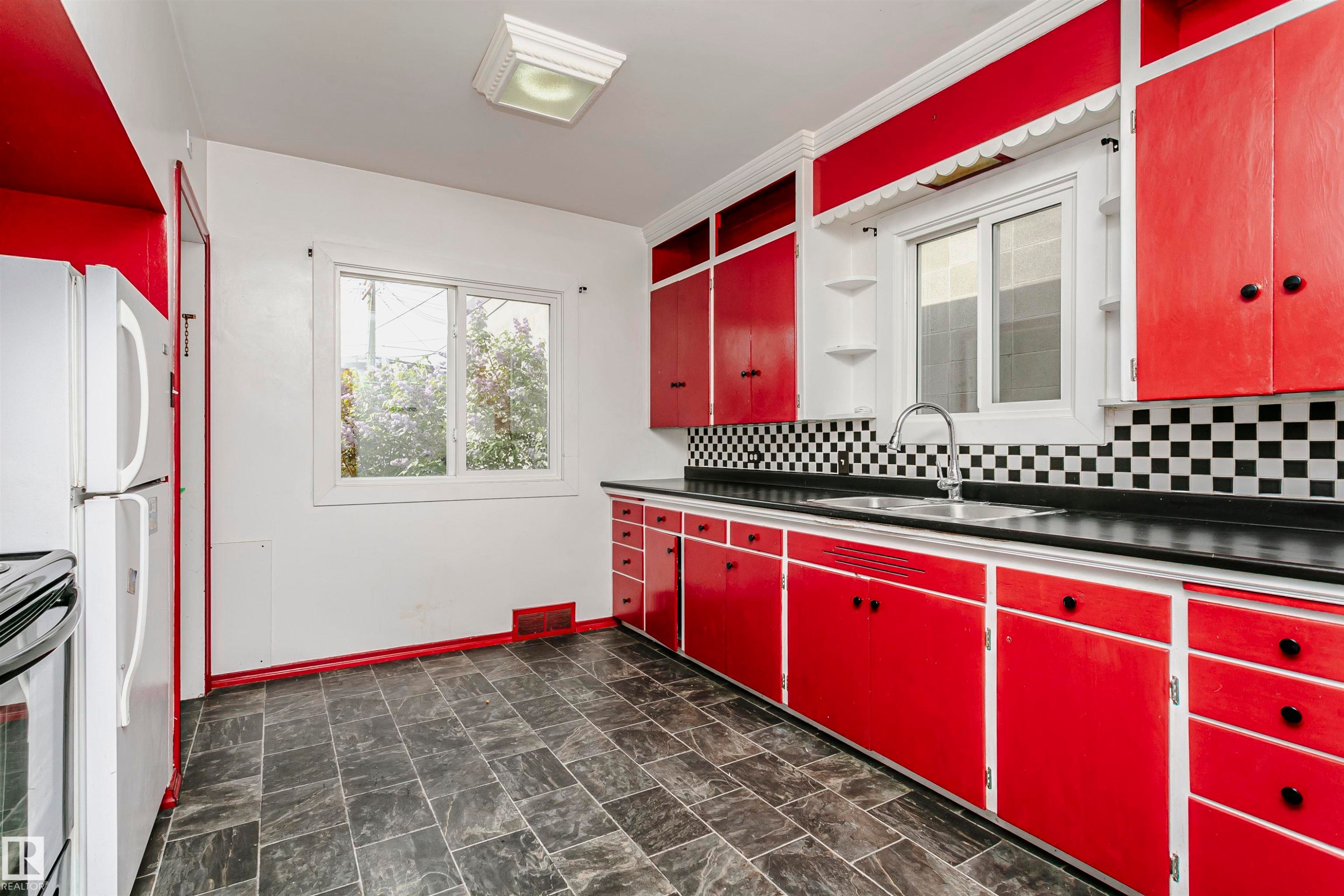 Kitchen featuring red cabinetry, black countertops, checkerboard tile backsplash, and a double-basin stainless steel sink with a gooseneck faucet - 10035 81 Avenue Nw, Edmonton, AB - Indoor Photo Showing Other Room