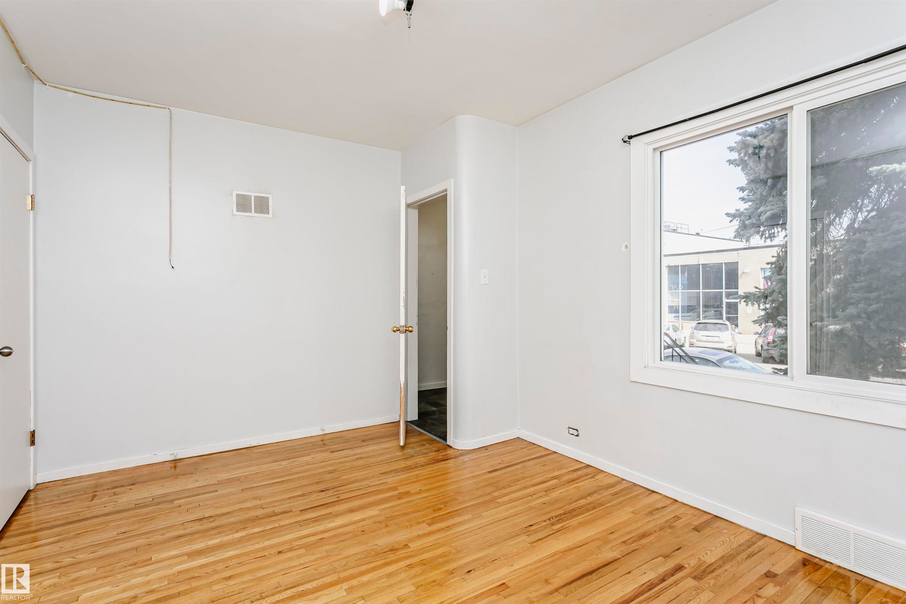 Room featuring wood-finish flooring, white baseboards, and a large window with a white frame - 10035 81 Avenue Nw, Edmonton, AB - Indoor Photo Showing Other Room