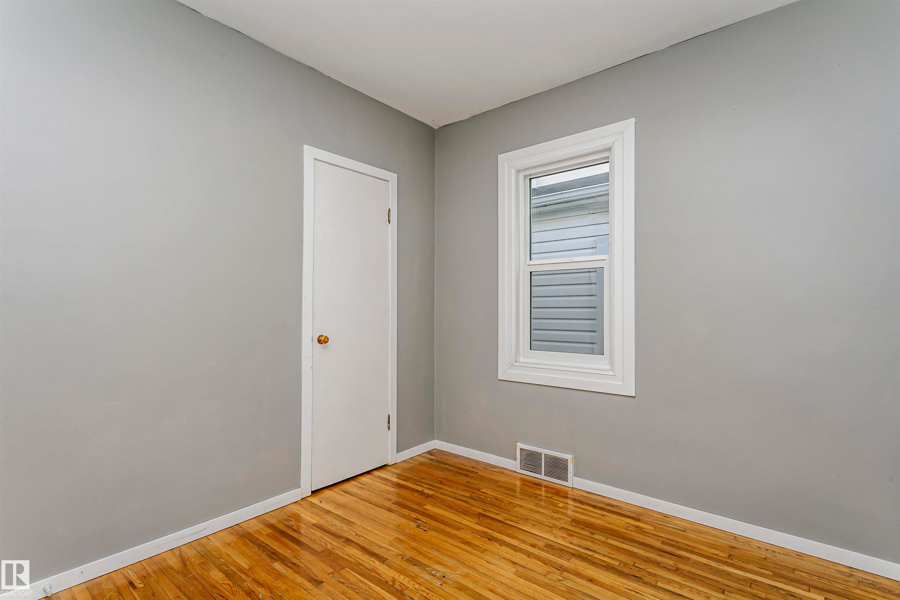 Bright room featuring wood-finish flooring, light grey painted walls, a white trim window, and a white interior door - 10035 81 Avenue Nw, Edmonton, AB - Indoor Photo Showing Other Room
