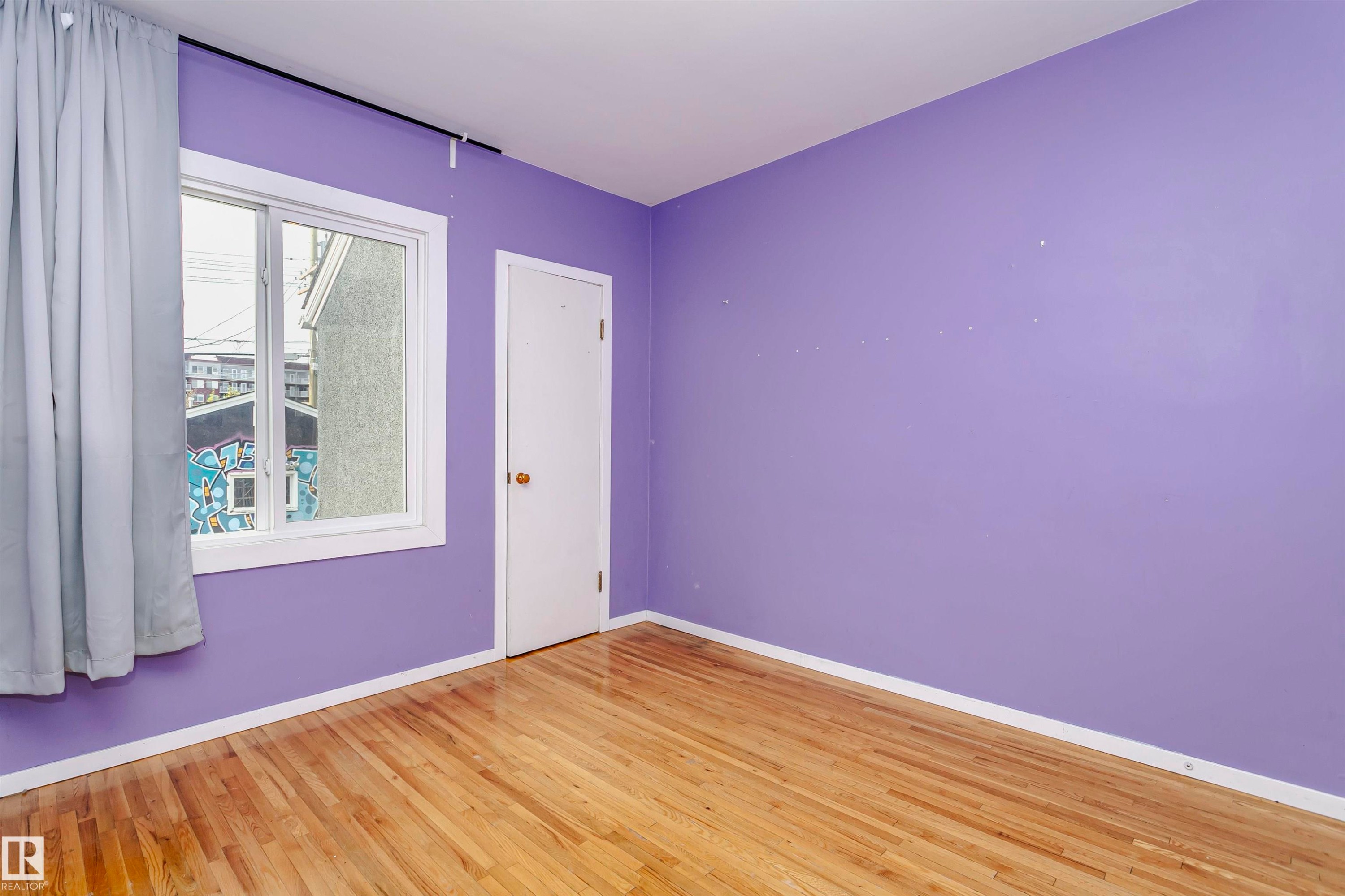 Bright room with wood-finish flooring, a white trim baseboard, a window with a white frame, and a white door with a brass-finish knob - 10035 81 Avenue Nw, Edmonton, AB - Indoor Photo Showing Other Room