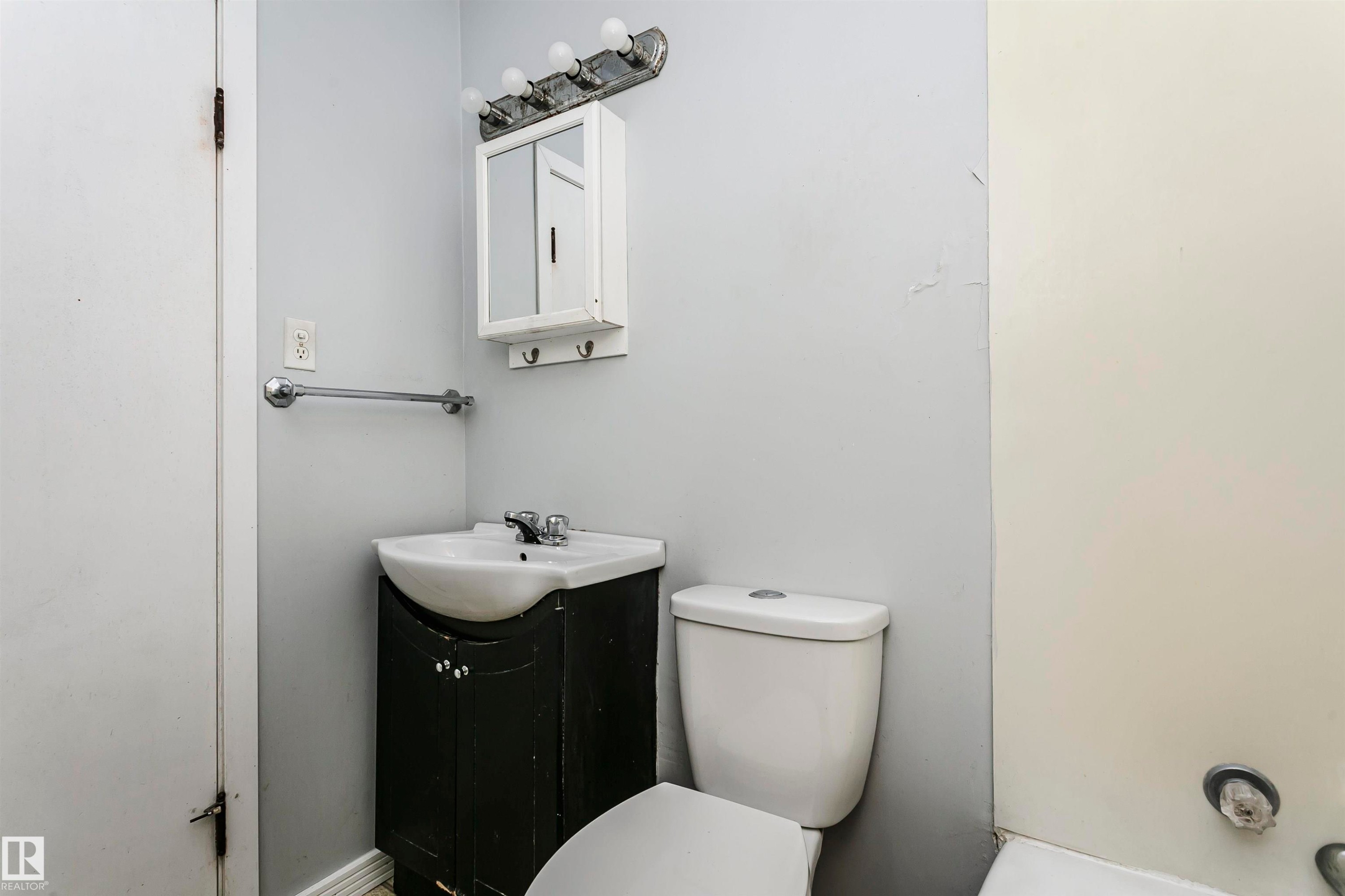 Compact bathroom featuring a white porcelain sink, dark wood-finish vanity, wall-mounted medicine cabinet, and a chrome towel bar - 10035 81 Avenue Nw, Edmonton, AB - Indoor Photo Showing Bathroom