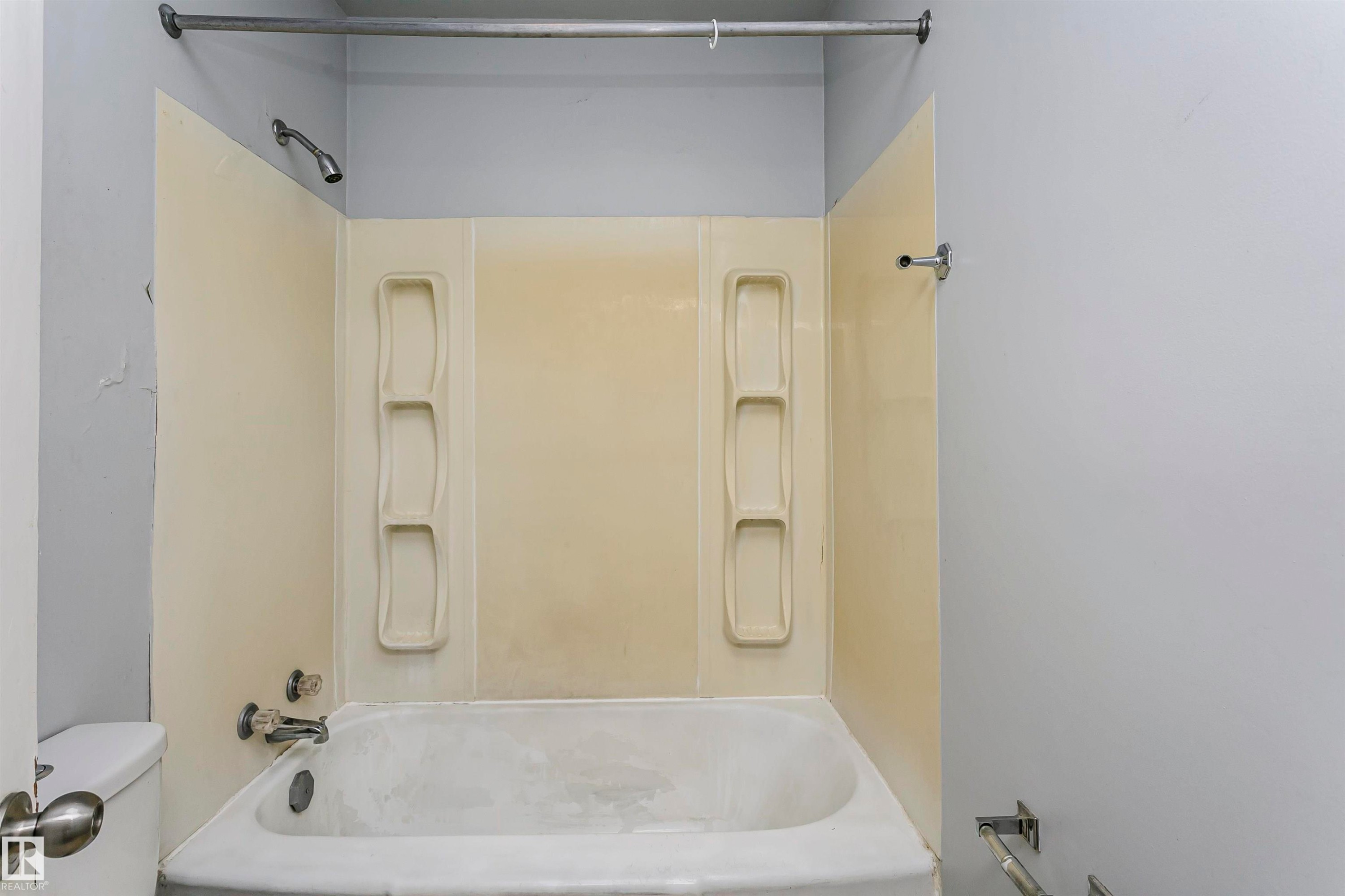 White bathtub with integrated shower, cream-colored wall surround, and built-in shelving - 10035 81 Avenue Nw, Edmonton, AB - Indoor Photo Showing Bathroom