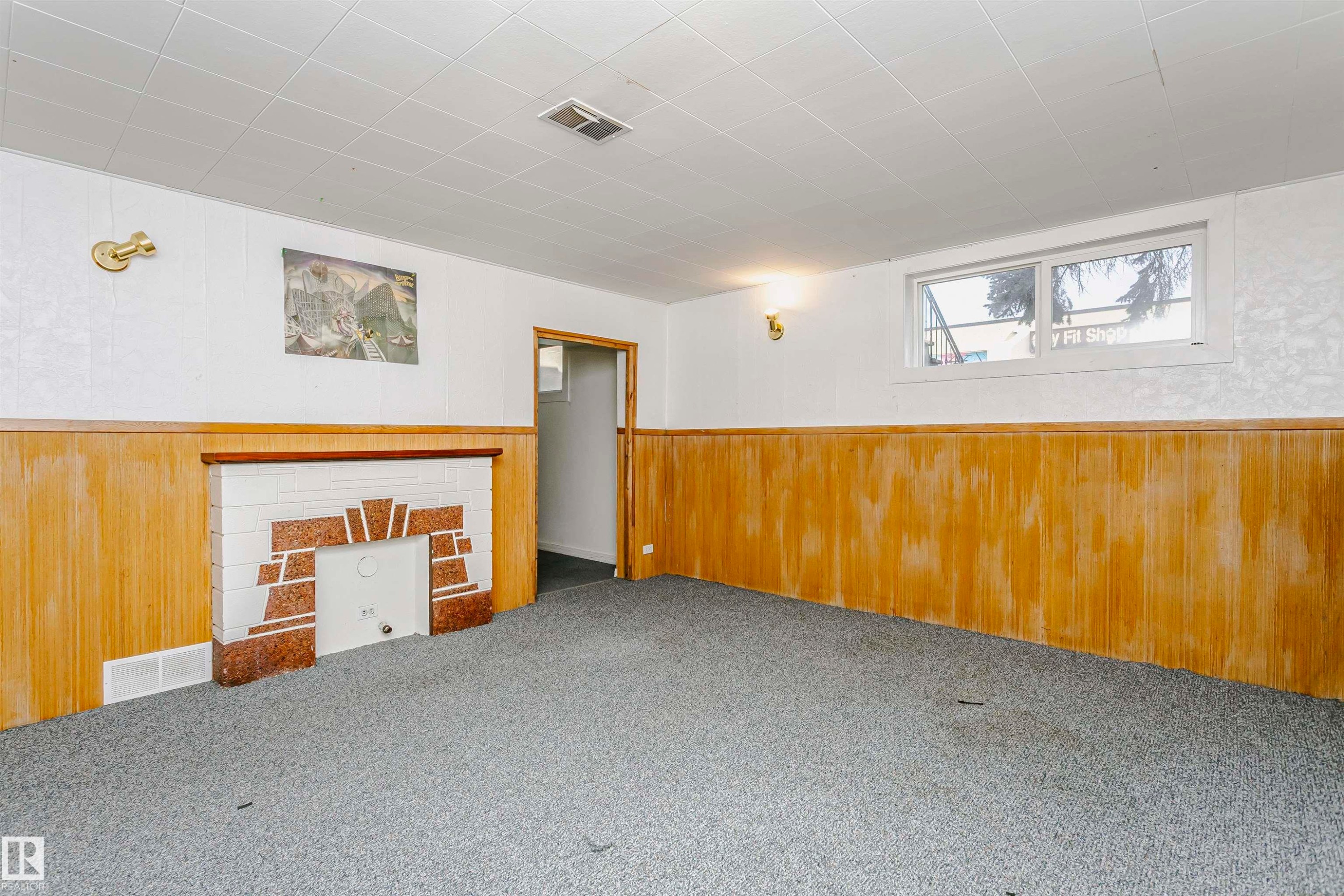 Finished interior space featuring a decorative fireplace with white and red-toned stone accents, wood-finish paneling, and a window providing natural illumination - 10035 81 Avenue Nw, Edmonton, AB - Indoor Photo Showing Other Room