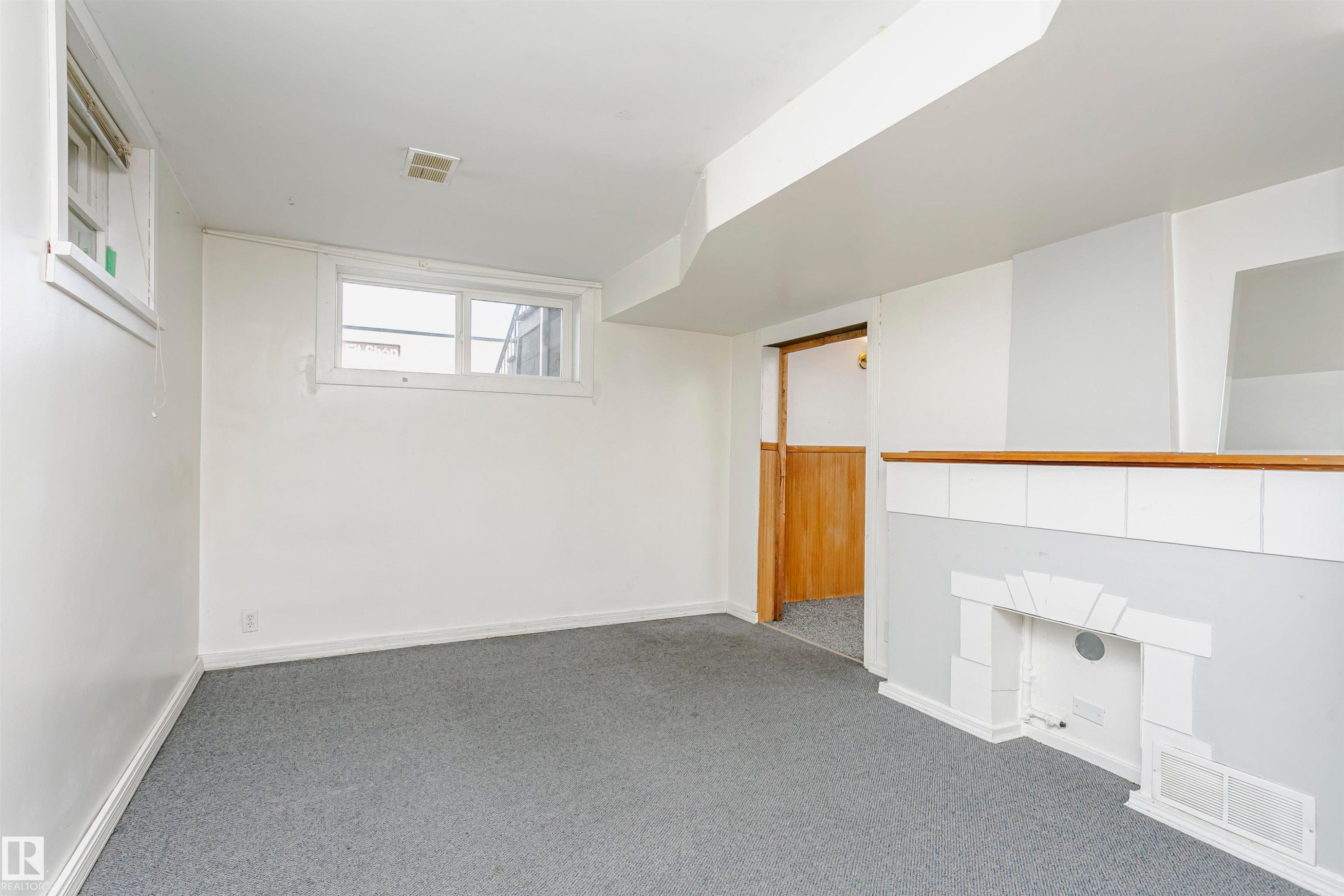 Carpeted room with a decorative fireplace feature, a wood-paneled doorway, and two windows providing natural light - 10035 81 Avenue Nw, Edmonton, AB - Indoor