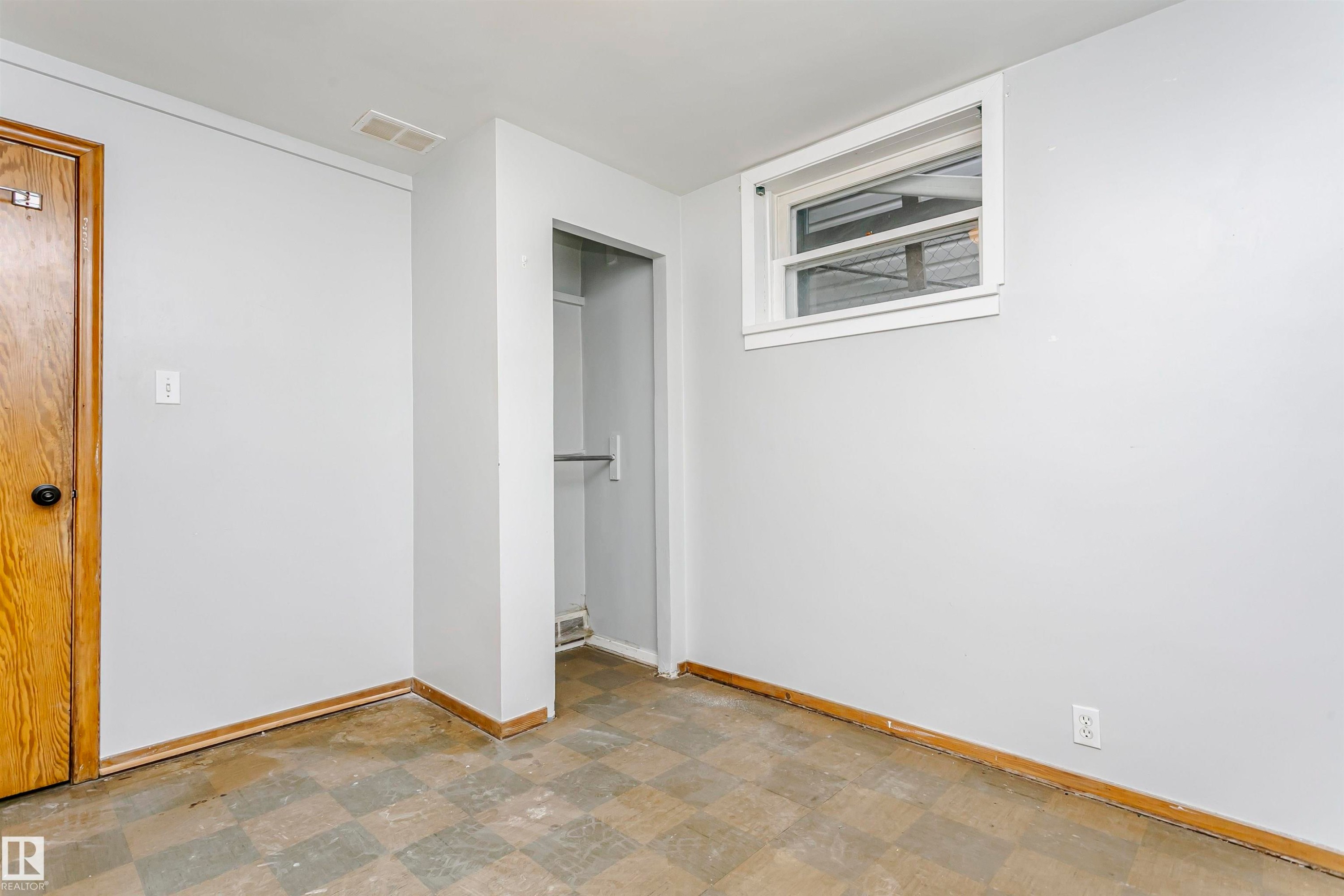 Interior room featuring a window, wood-finish door, open closet space with a hanging rod, light-colored walls, and checkered floor tiles - 10035 81 Avenue Nw, Edmonton, AB - Indoor Photo Showing Other Room