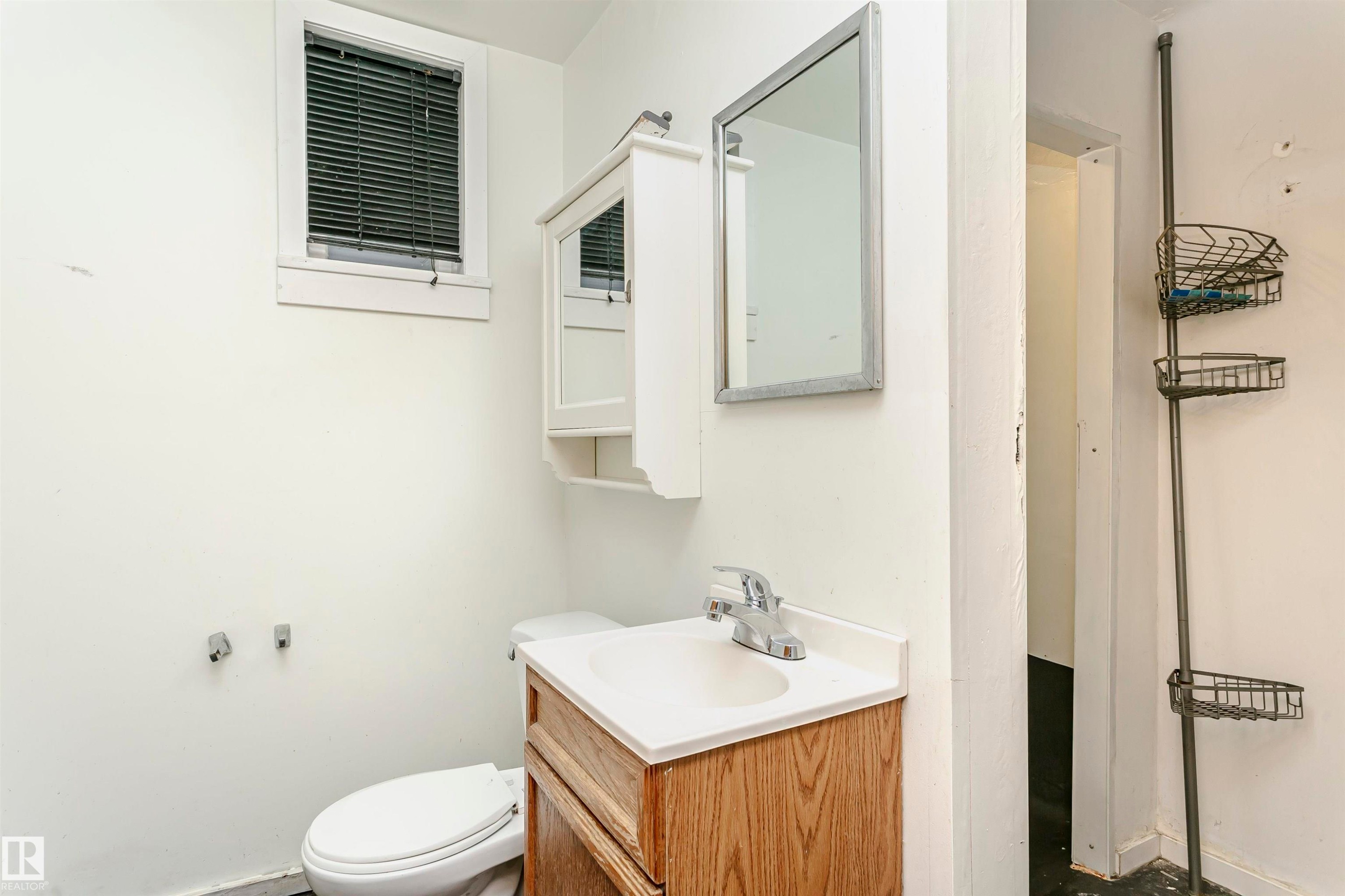 Bathroom featuring a window with blinds, a wood-finish vanity with an integrated sink, a framed mirror, and a wall-mounted medicine cabinet - 10035 81 Avenue Nw, Edmonton, AB - Indoor Photo Showing Bathroom