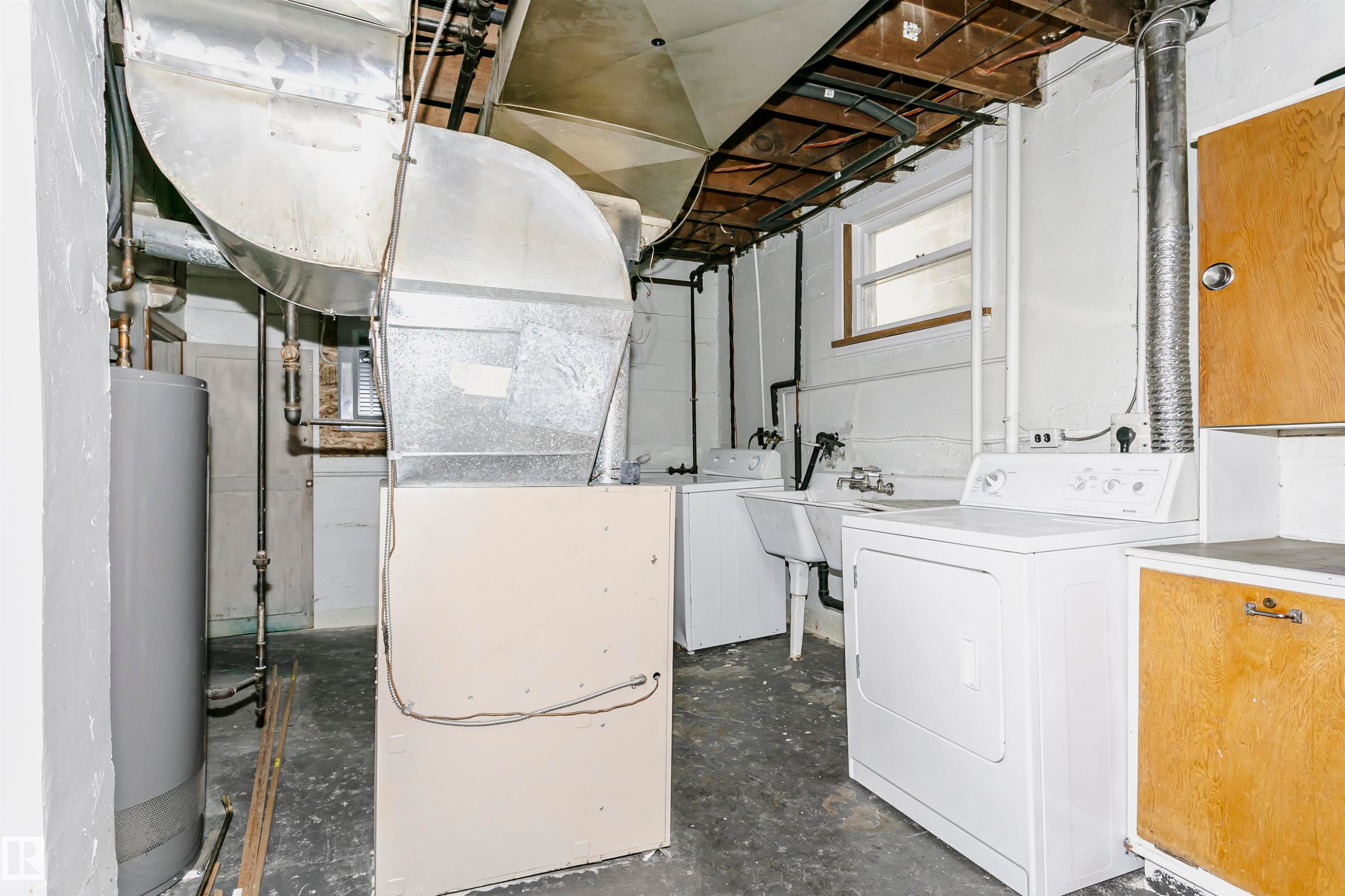 Basement utility area featuring a hot water heater, large galvanized HVAC ductwork, and exposed ceiling joists - 10035 81 Avenue Nw, Edmonton, AB - Indoor Photo Showing Laundry Room
