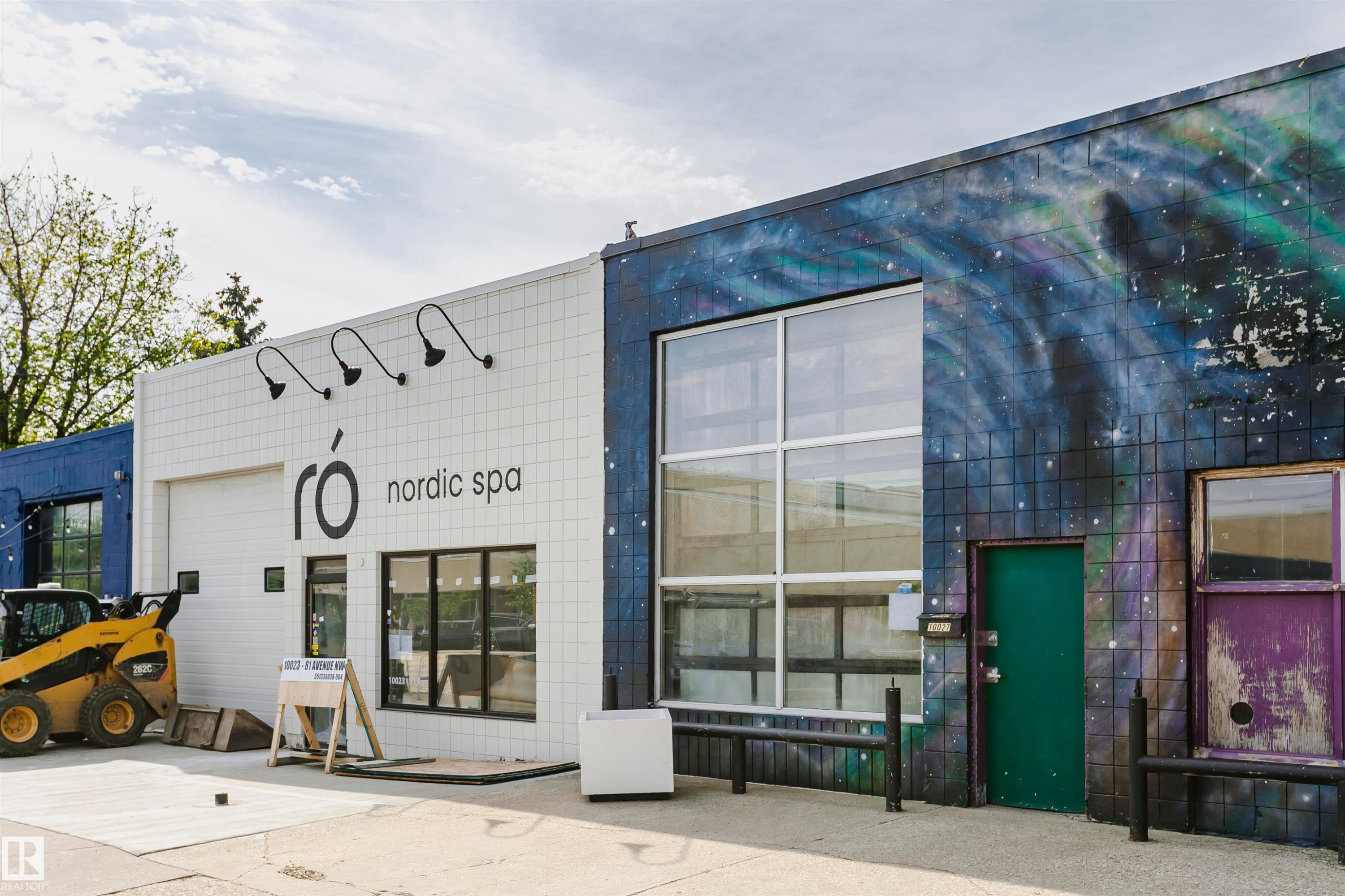 Commercial storefront featuring white square tile facade, prominent business signage, and gooseneck exterior lighting fixtures - 10035 81 Avenue Nw, Edmonton, AB - Outdoor