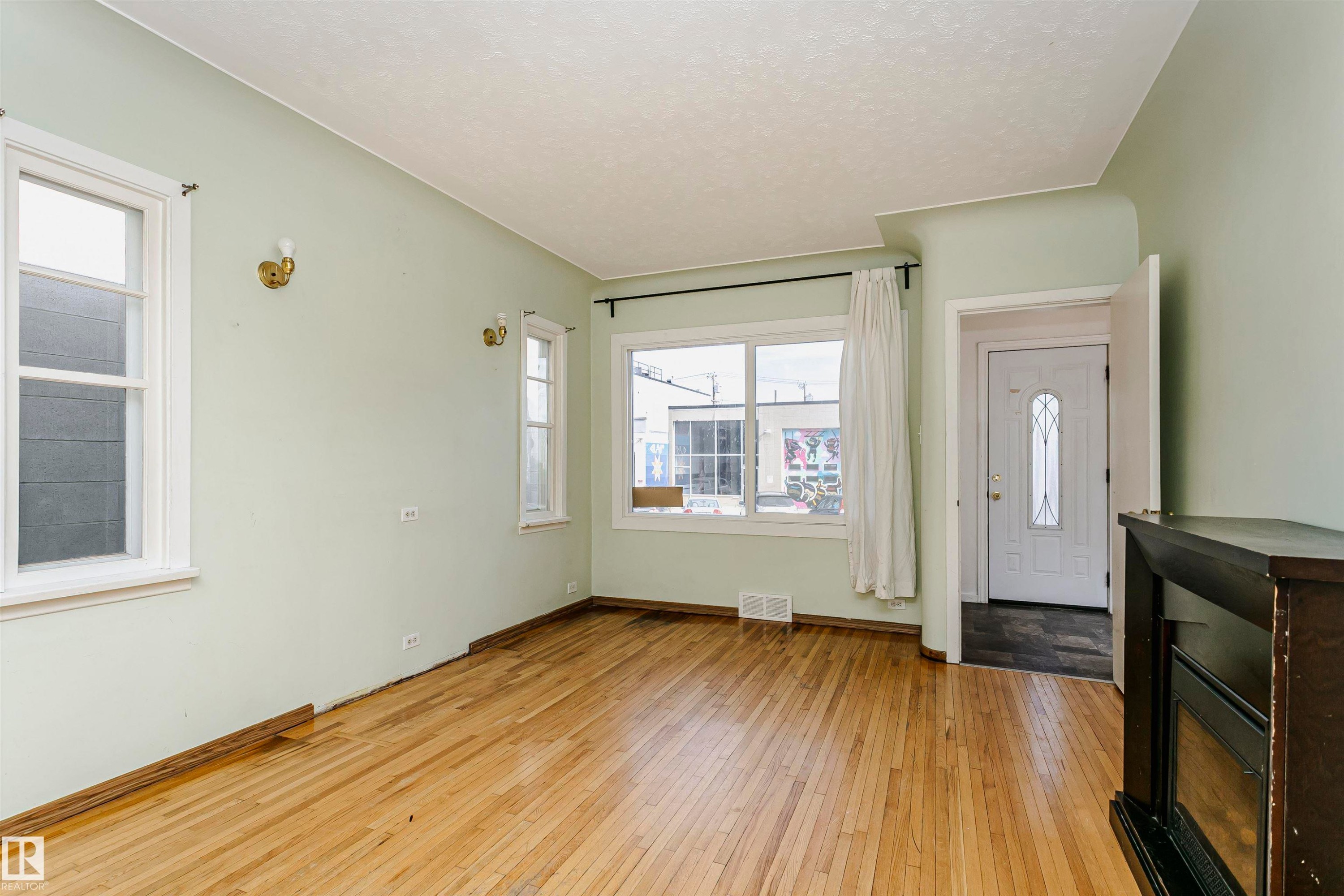 Hardwood-style flooring extends across this room, featuring light green walls and multiple windows with white trim - 10035 81 Avenue Nw, Edmonton, AB - Indoor Photo Showing Other Room