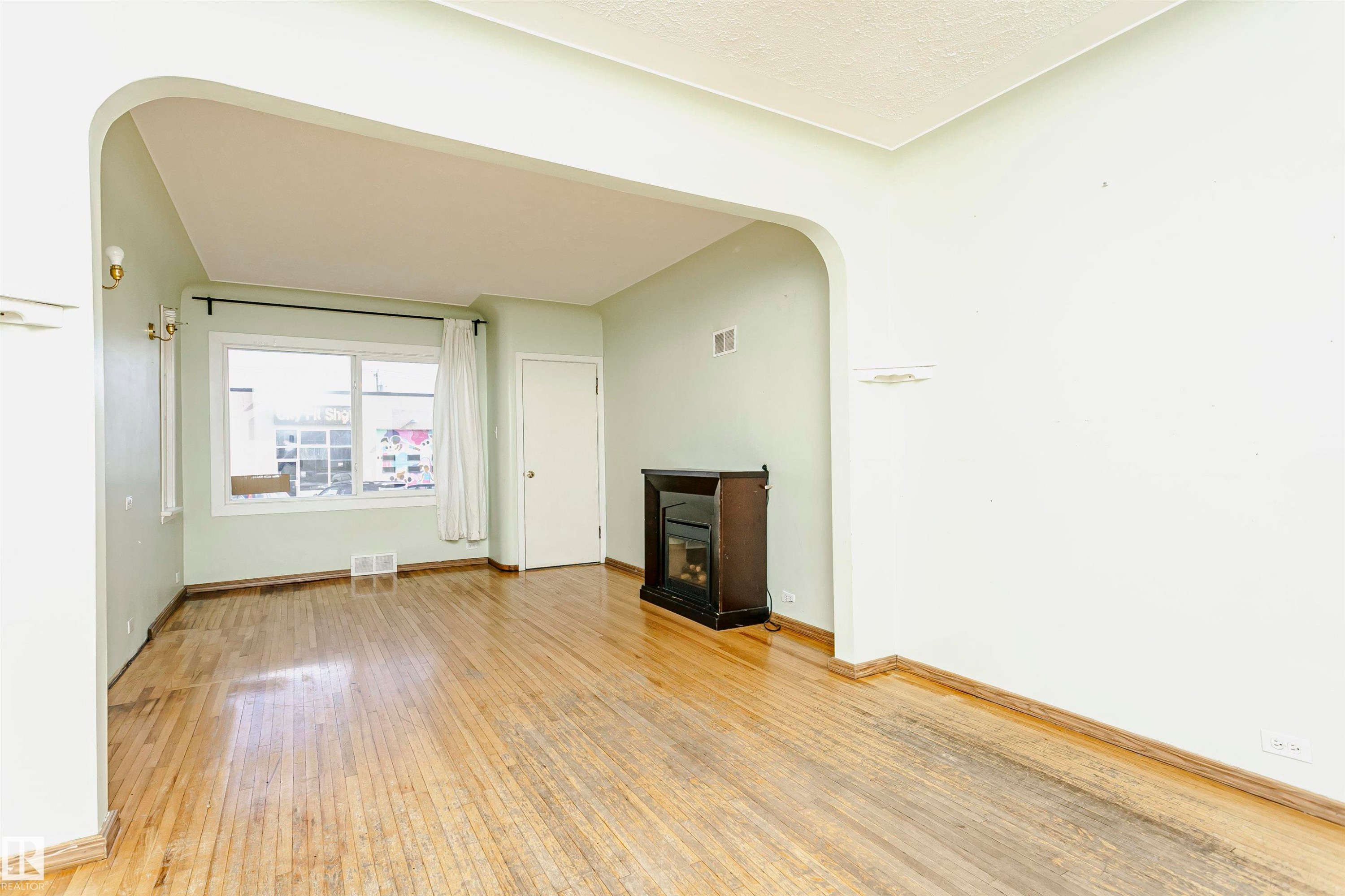 Spacious interior featuring wood-finish flooring, light-toned wall paint, and an arched doorway - 10035 81 Avenue Nw, Edmonton, AB - Indoor