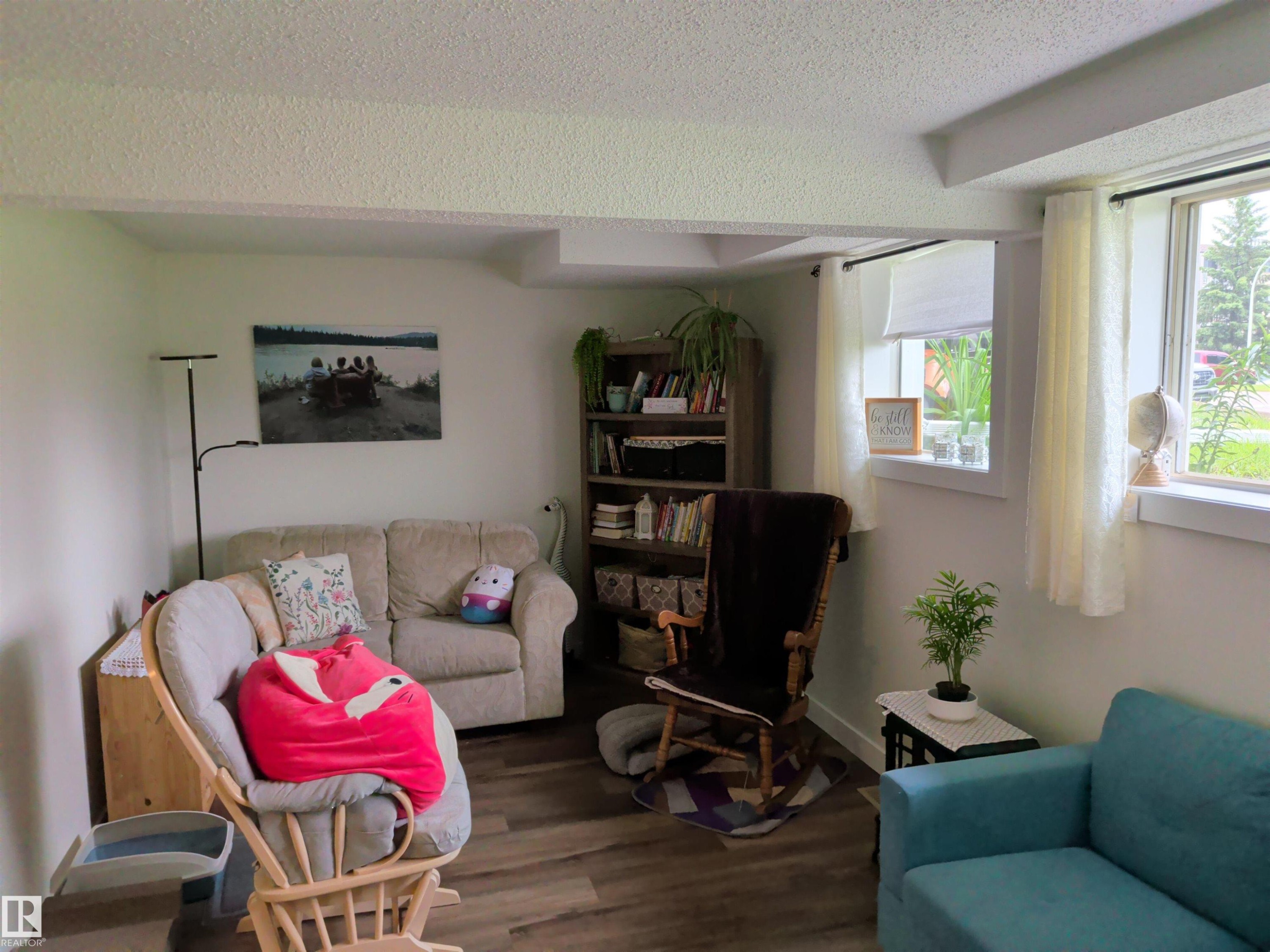 Living area featuring wood-finish flooring, two large windows, a built-in bookshelf, and a neutral color palette - 31 Brown Street, Stony Plain, AB