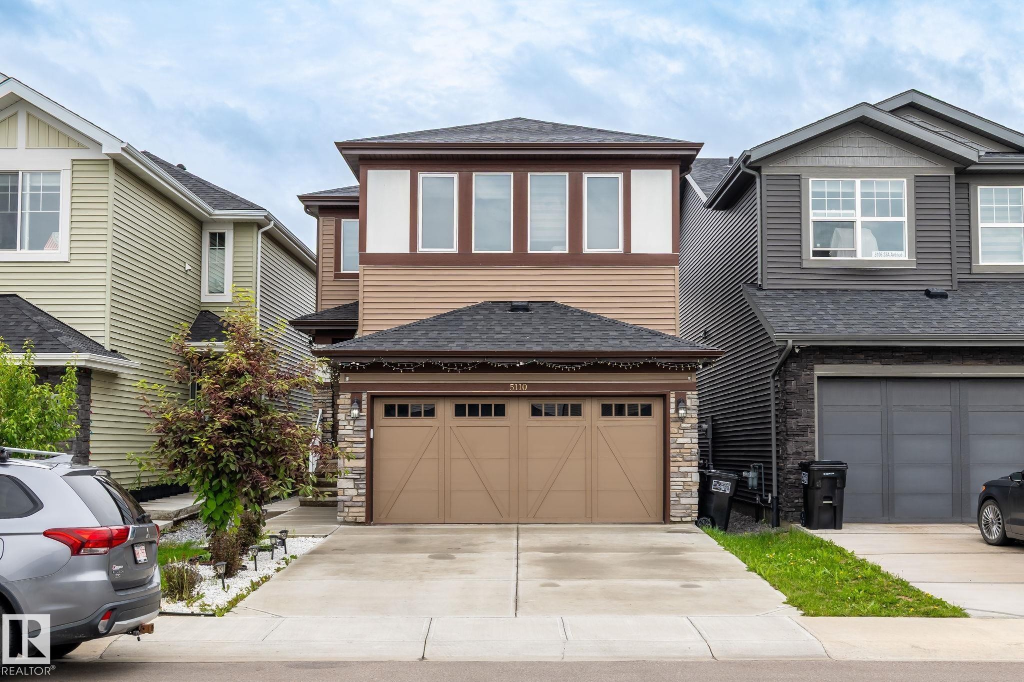 Two-story exterior with a two-car garage, stone accents, horizontal siding, and a prominent upper-level window bank - 5110 23A Ave Sw, Edmonton, AB