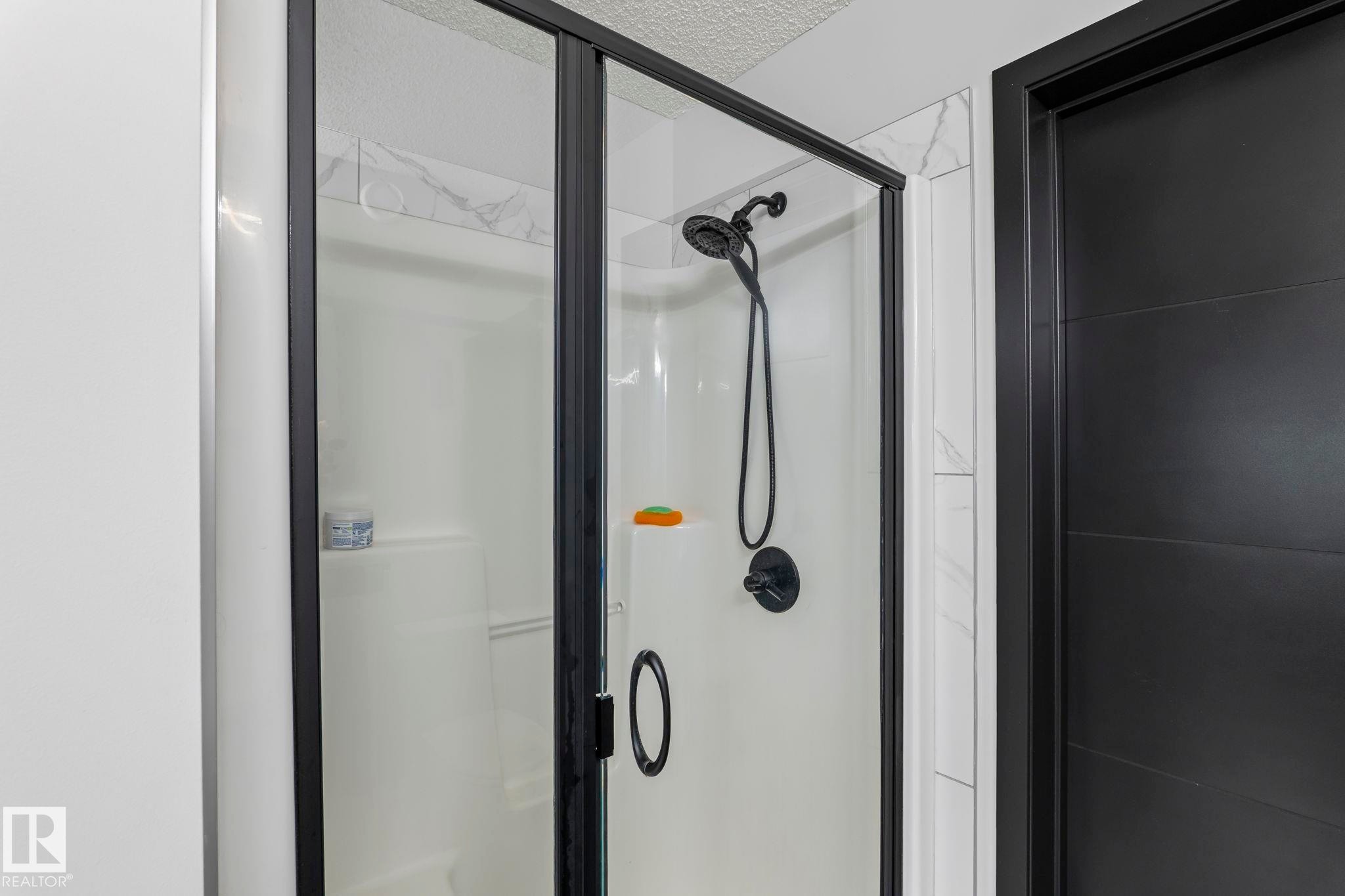 Shower enclosure with black-framed glass doors, white shower pan, and matte black shower fixtures - 5110 23A Ave Sw, Edmonton, AB