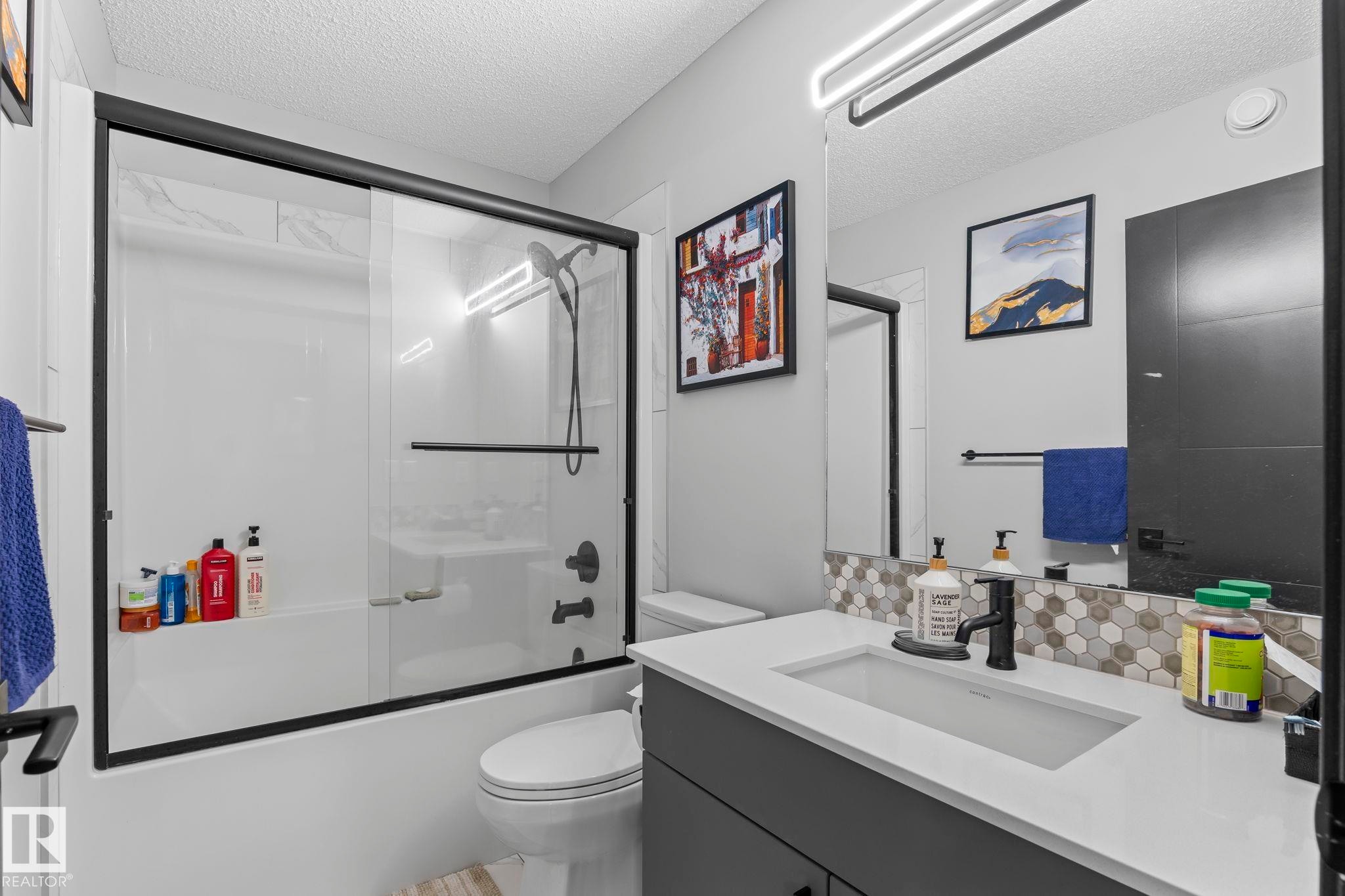 Bathroom featuring a shower-tub combination with black-framed sliding glass doors, black plumbing fixtures, and white subway tile surround - 5110 23A Ave Sw, Edmonton, AB
