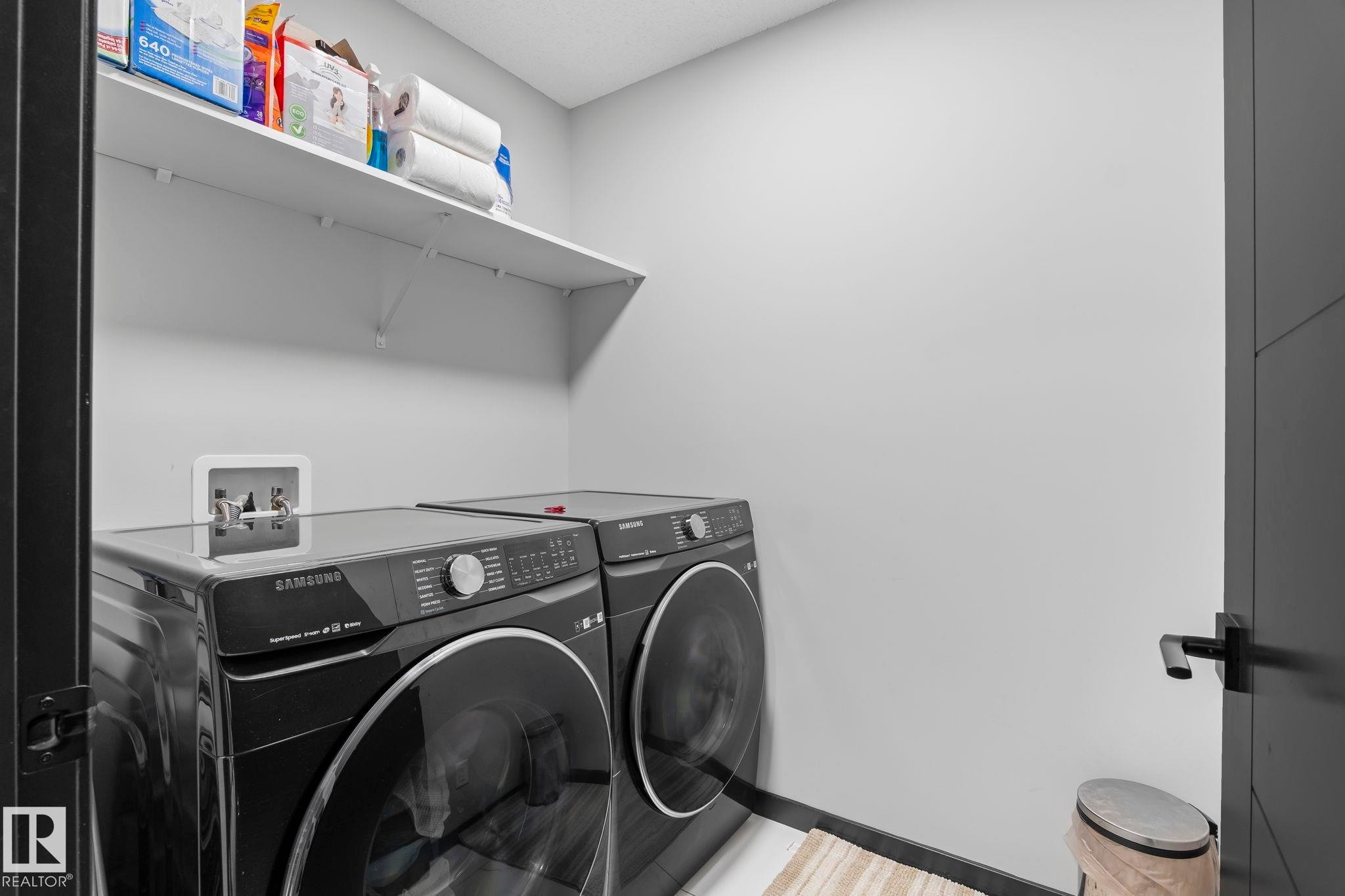Dedicated laundry area featuring a wall-mounted shelf, light-toned walls, and dark-toned base trim - 5110 23A Ave Sw, Edmonton, AB