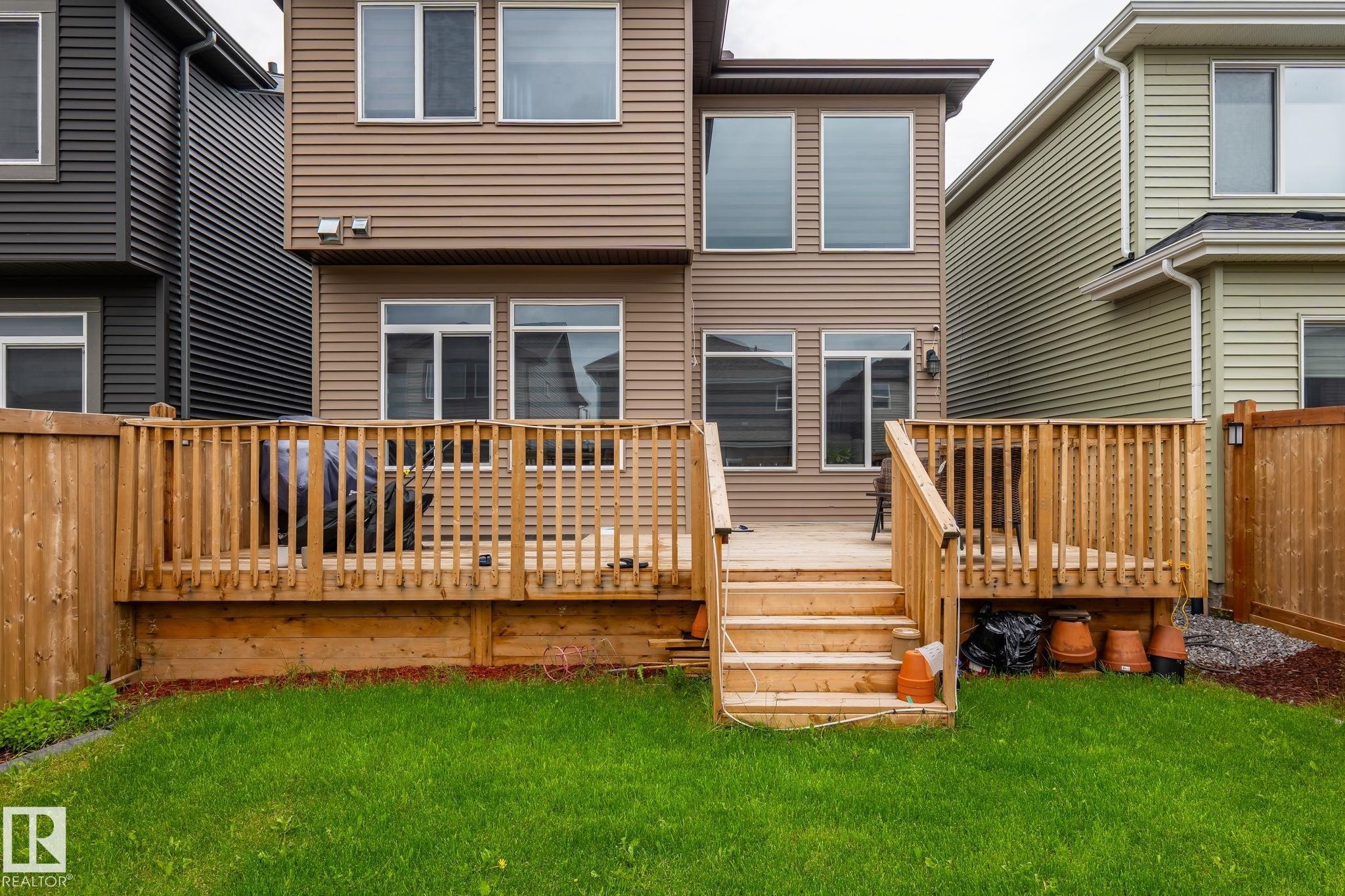 Expansive backyard featuring a multi-level wooden deck with baluster railings and steps descending to a grassy lawn - 5110 23A Ave Sw, Edmonton, AB