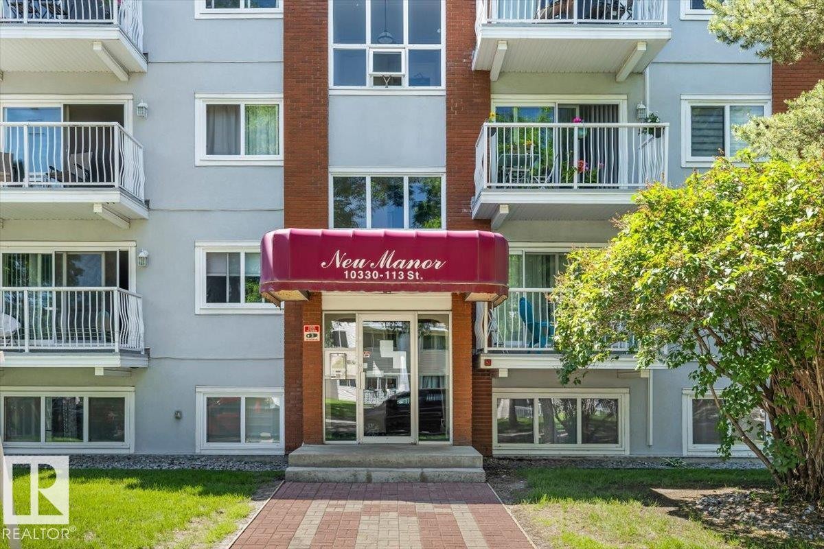 Multi-story building exterior featuring a red brick facade, light grey siding, and multiple balconies with white railings - #202 10330 113 St Nw, Edmonton, AB