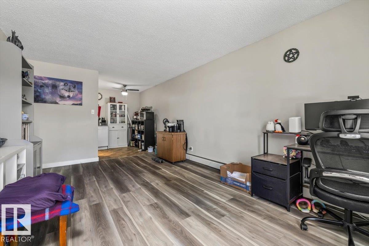 Spacious interior with wood-finish flooring, light neutral wall tones, and a textured white ceiling - #202 10330 113 St Nw, Edmonton, AB