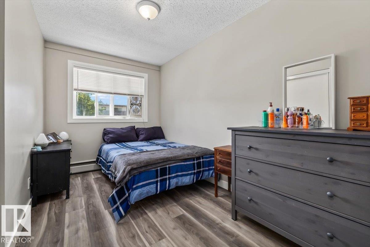 Room featuring wood-finish flooring, a window with blinds, and light-toned walls - #202 10330 113 St Nw, Edmonton, AB