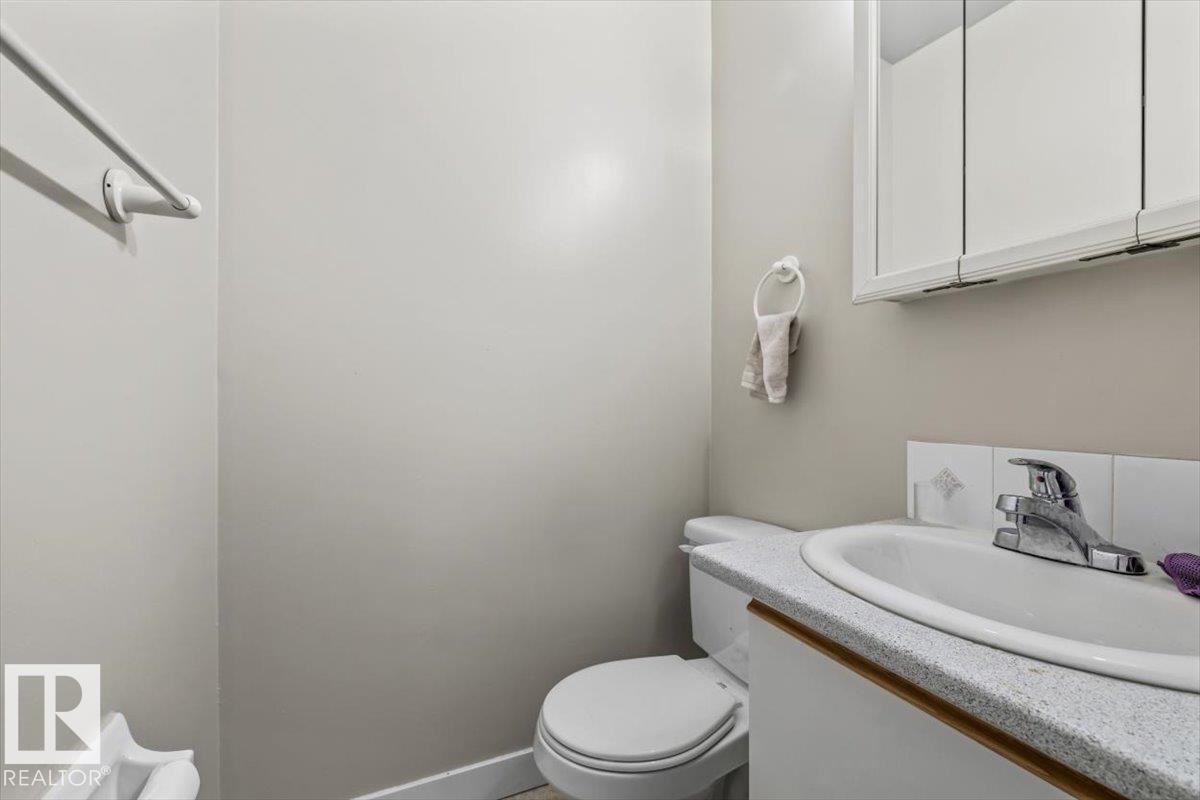 Bathroom featuring a white toilet, a vanity with a white countertop and integrated sink, a chrome faucet, and a wall-mounted mirrored medicine cabinet - #202 10330 113 St Nw, Edmonton, AB
