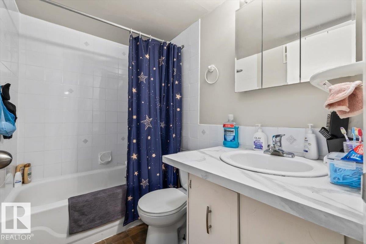 Bathroom featuring a white bathtub with tile surround, vanity with an integrated sink, and a mirrored medicine cabinet - #202 10330 113 St Nw, Edmonton, AB