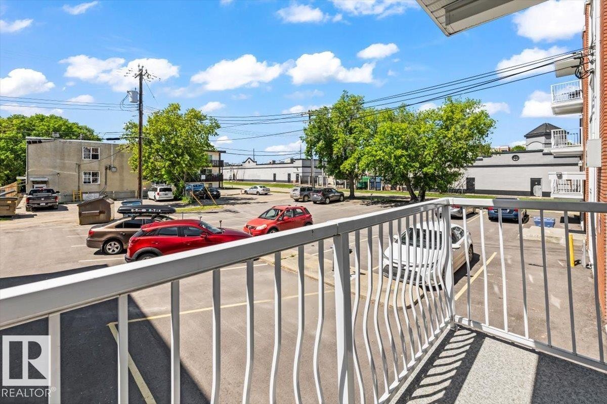 Balcony with white metal railing and a concrete surface, overlooking a paved parking area - #202 10330 113 St Nw, Edmonton, AB