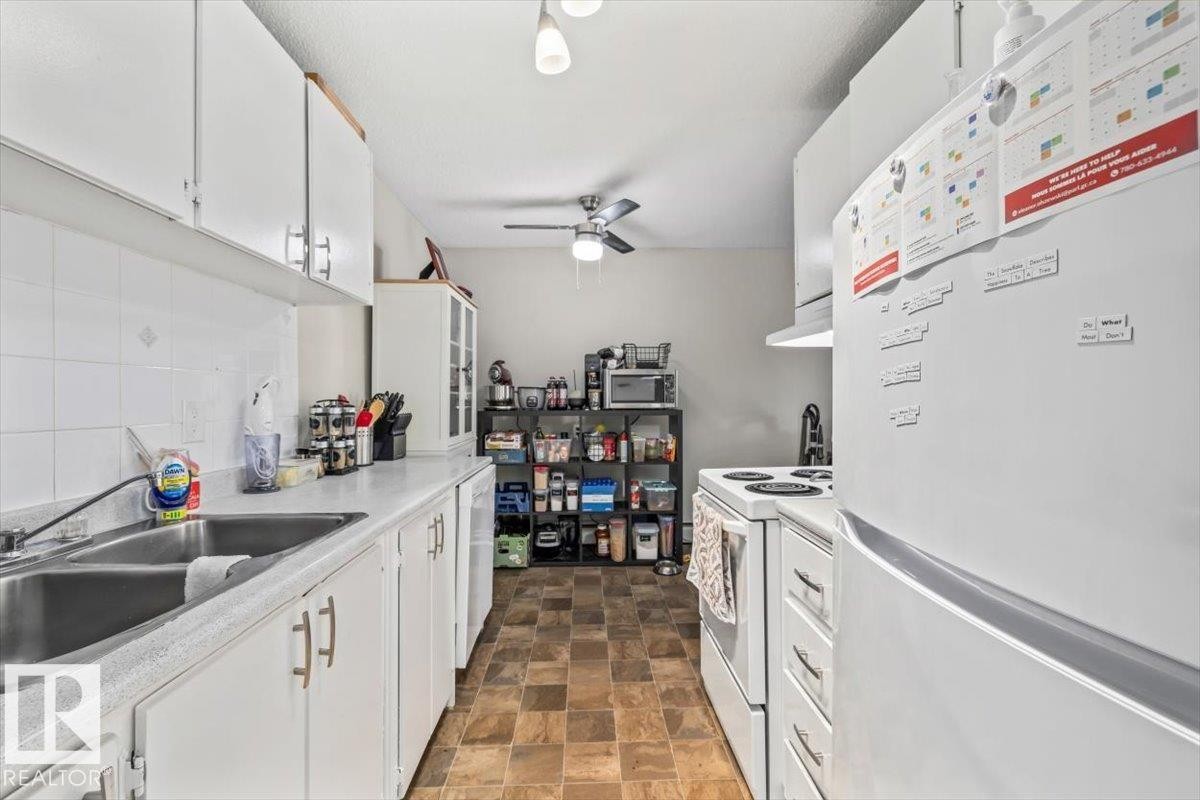 Galley kitchen featuring white cabinetry, a double basin stainless steel sink, white countertops, and a white tile backsplash - #202 10330 113 St Nw, Edmonton, AB