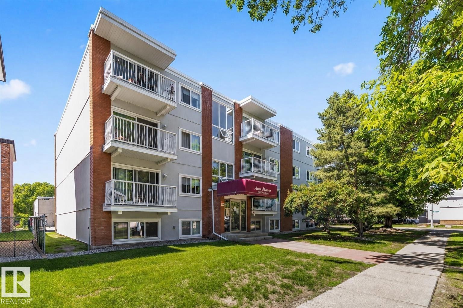 Multi-story residential building featuring a light gray facade with brick accents and multiple private balconies with white railings - #306 10330 113 St Nw, Edmonton, AB