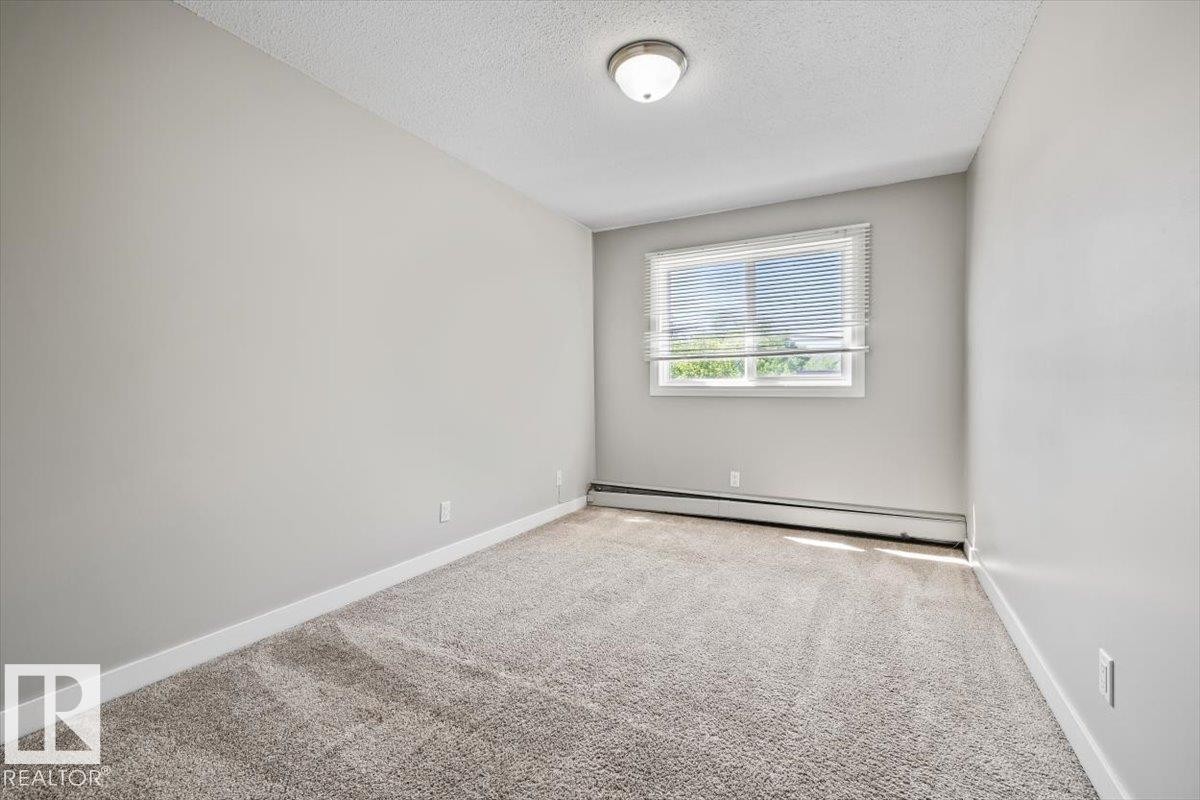 Carpeted room with light neutral wall paint, white trim, a single window with blinds, and a flush-mount ceiling light fixture - #306 10330 113 St Nw, Edmonton, AB