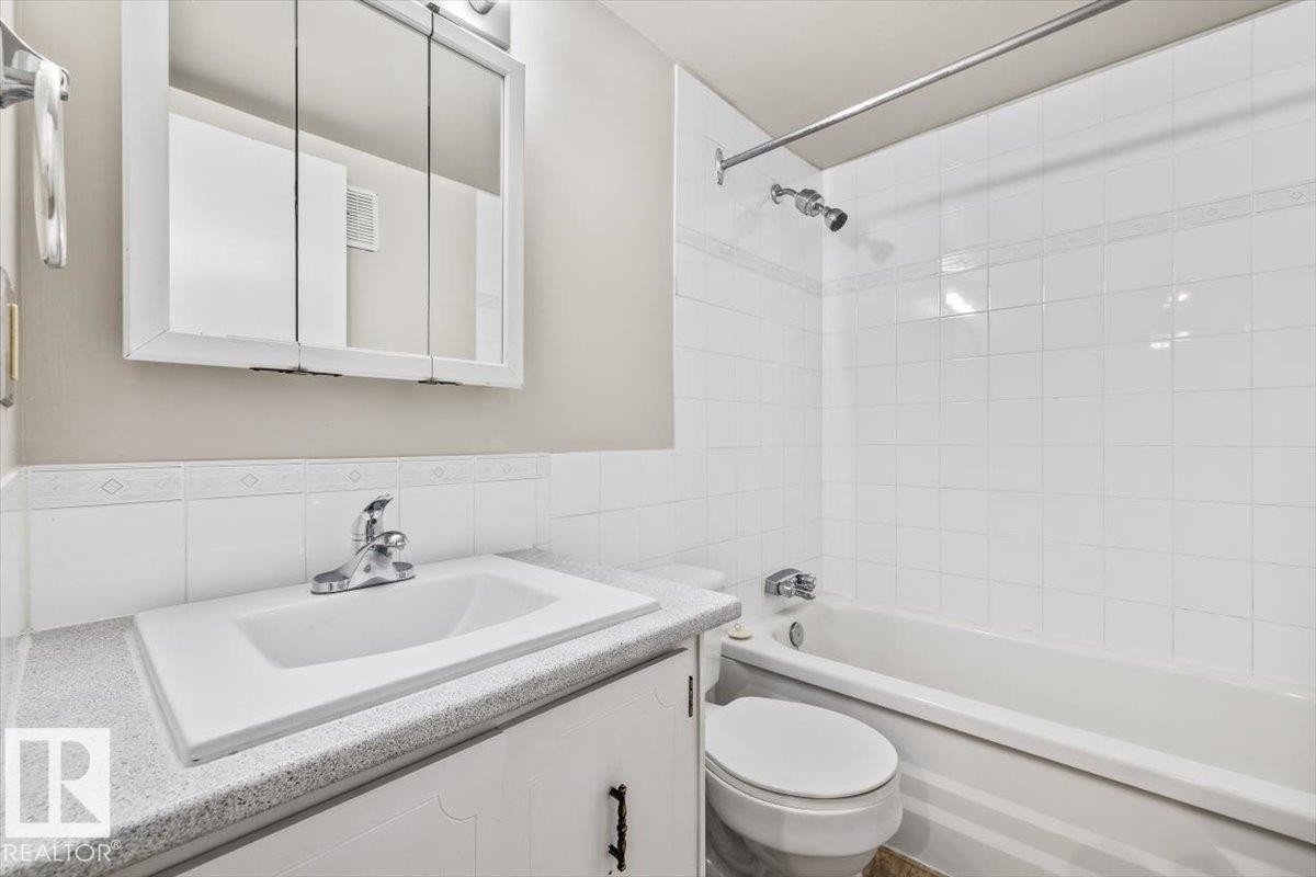 Bathroom featuring a white vanity with a light-colored countertop, an integrated sink, and a mirrored medicine cabinet - #306 10330 113 St Nw, Edmonton, AB