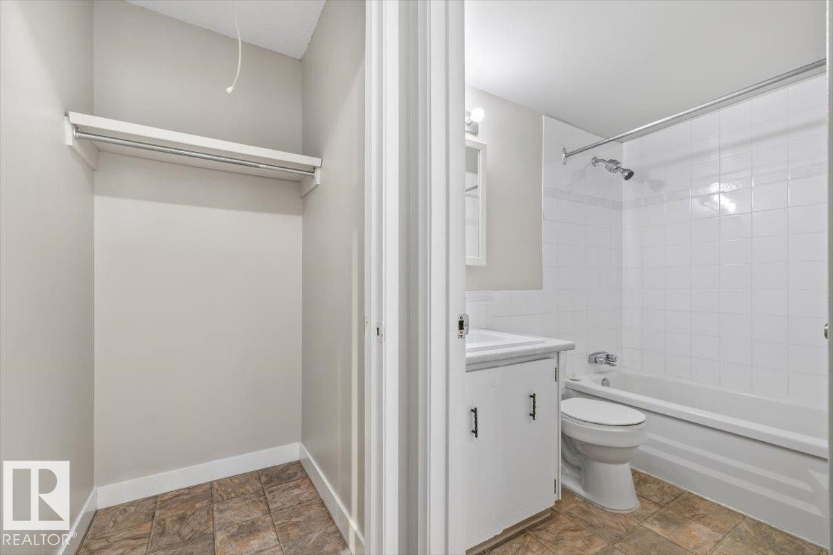 Bathroom featuring a white vanity with integrated sink, chrome faucet, white tiled shower and tub combination, and ceramic tile flooring - #306 10330 113 St Nw, Edmonton, AB
