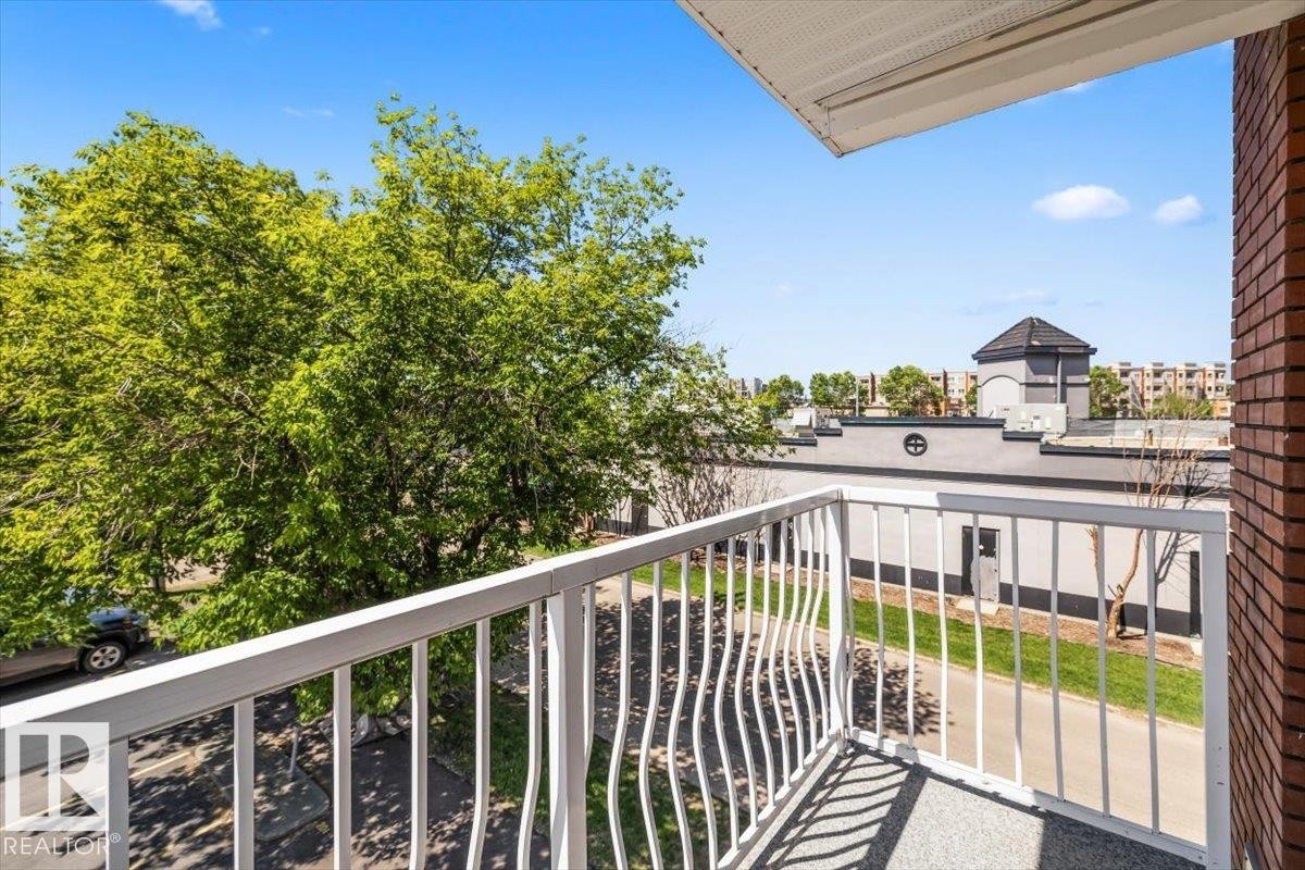 Exterior balcony featuring a textured floor, white metal railing, and brick wall - #306 10330 113 St Nw, Edmonton, AB