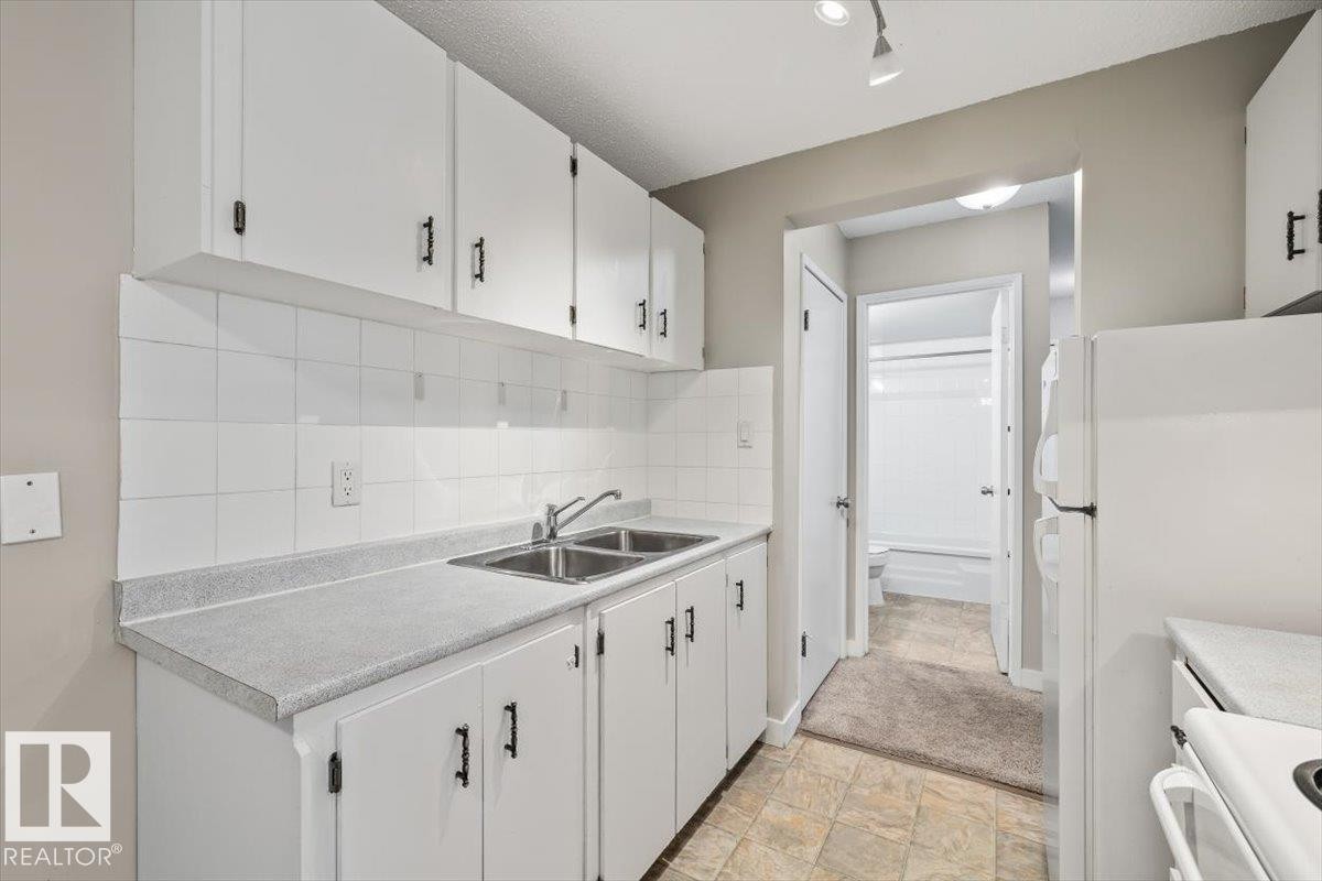 Kitchen featuring white cabinetry with dark hardware, a dual basin stainless steel sink, and light gray countertops - #306 10330 113 St Nw, Edmonton, AB