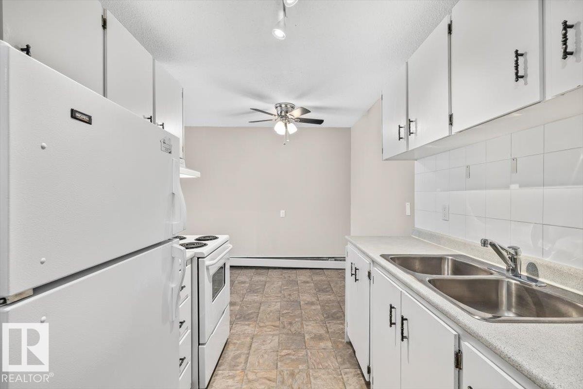 Efficient kitchen design featuring white cabinetry with dark hardware, white subway tile backsplash, and a double basin stainless steel sink - #306 10330 113 St Nw, Edmonton, AB