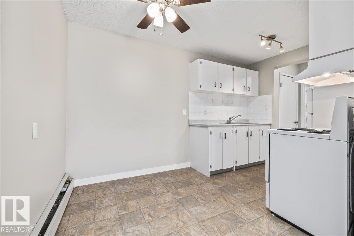 Open-concept kitchen and dining area featuring white cabinetry, a built-in sink, white tile backsplash, and patterned floor tiling - #306 10330 113 St Nw, Edmonton, AB