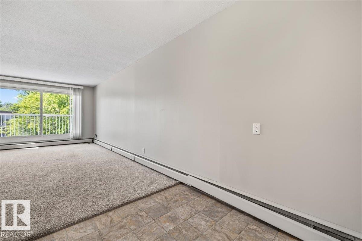 Bright living space featuring a full-width window with vertical blinds, providing abundant natural light - #306 10330 113 St Nw, Edmonton, AB