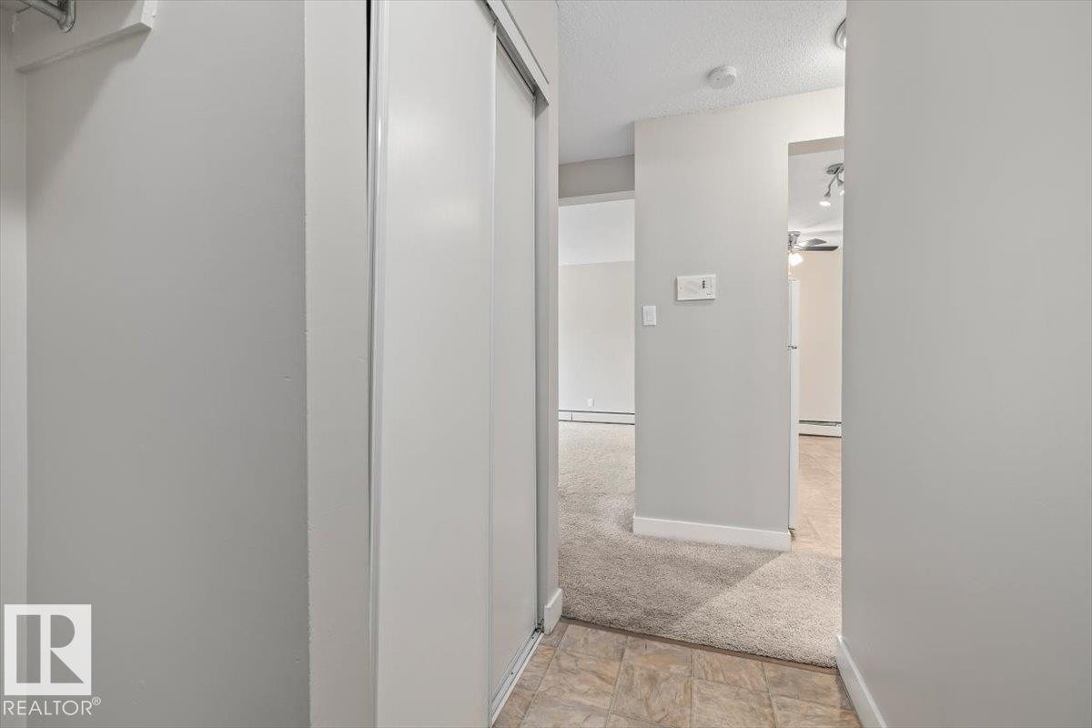 Hallway featuring light gray walls, white trim, and a sliding closet door - #306 10330 113 St Nw, Edmonton, AB