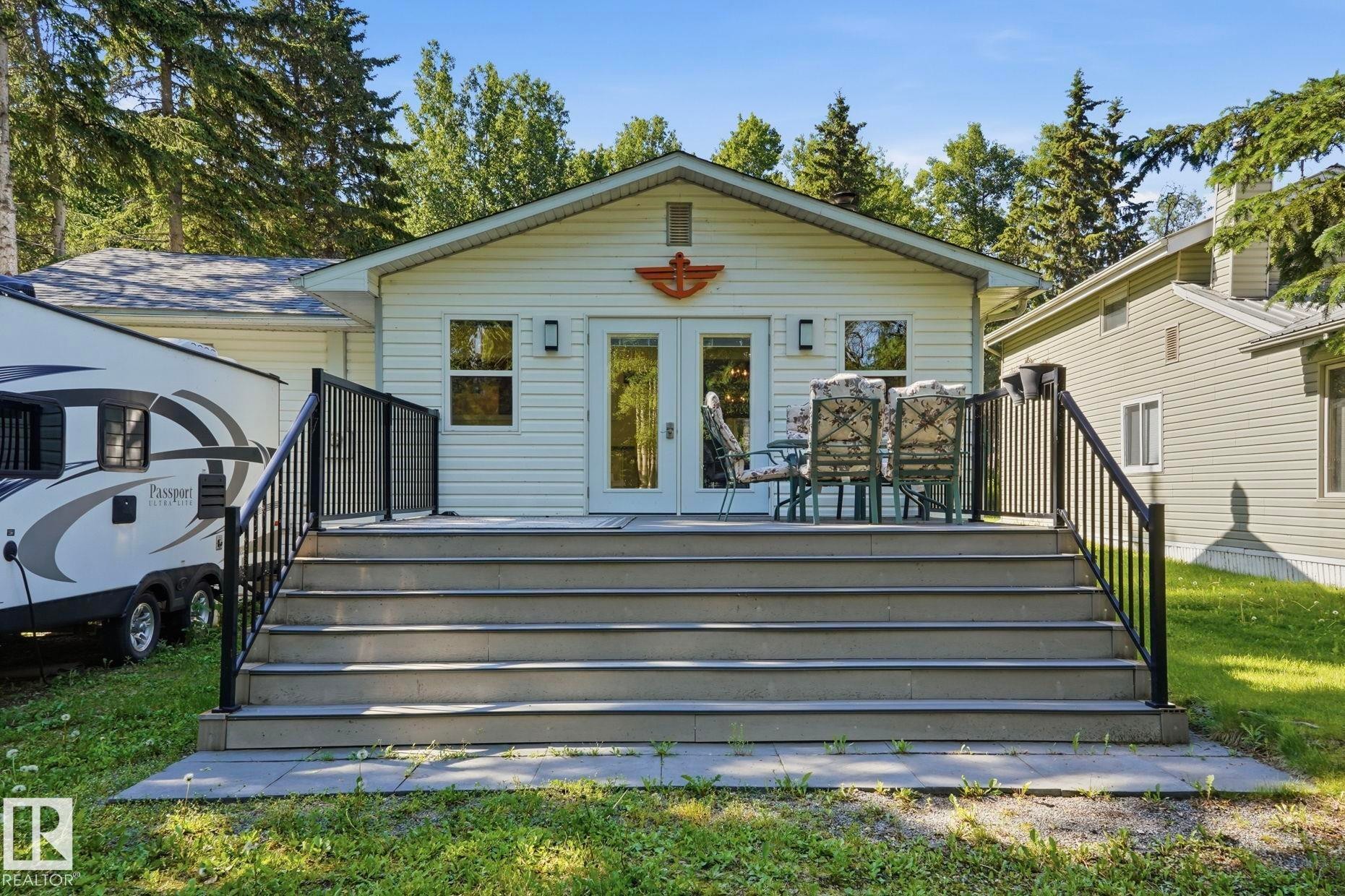 Rear exterior featuring white vinyl siding, a gabled roofline, a spacious deck with composite decking, black metal railings, and dual glass-paned doors - 1410 47436 Range Rd. 15, Rural Leduc County, AB
