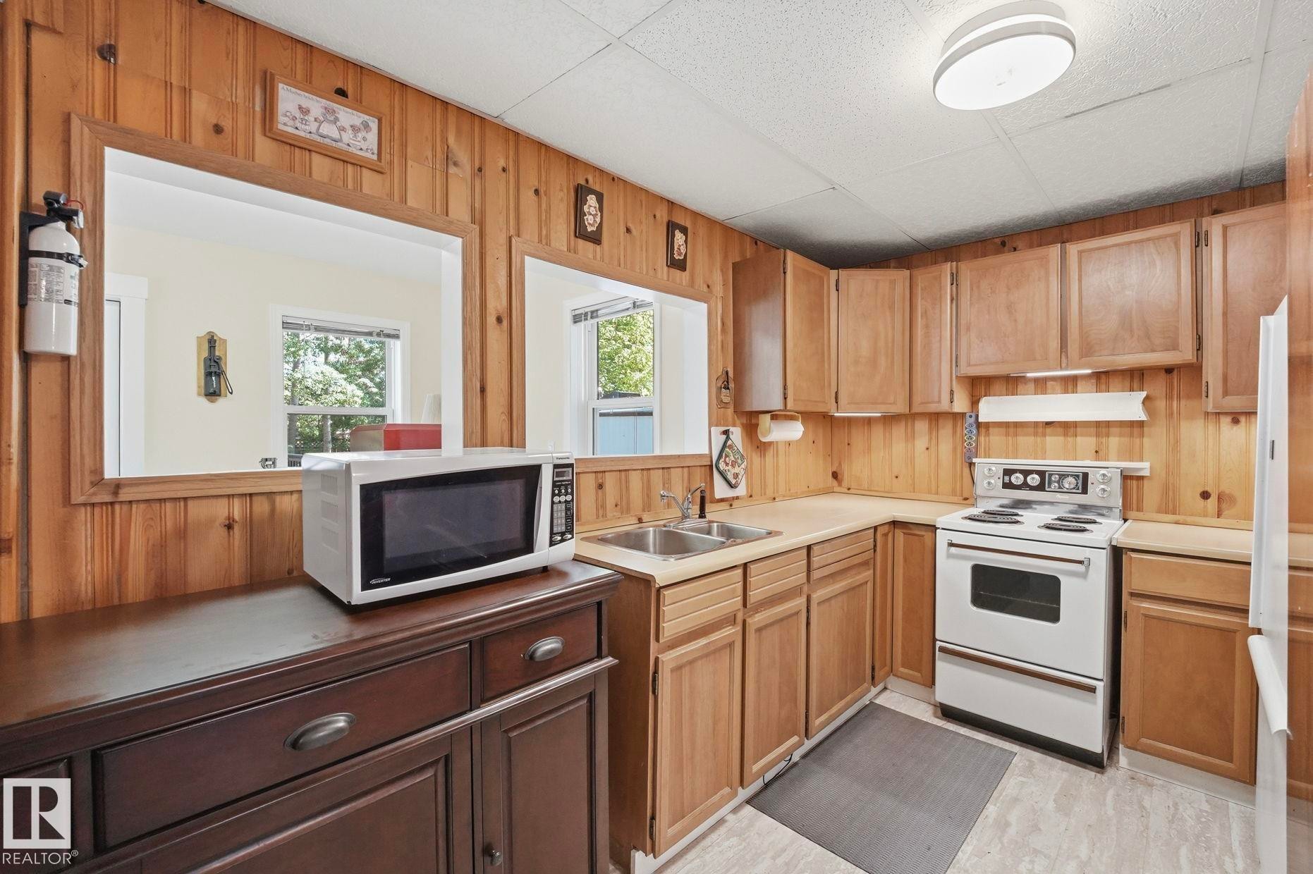 Kitchen featuring wood paneling, light wood cabinetry, a double basin stainless steel sink, and a white electric range with matching hood - 1410 47436 Range Rd. 15, Rural Leduc County, AB