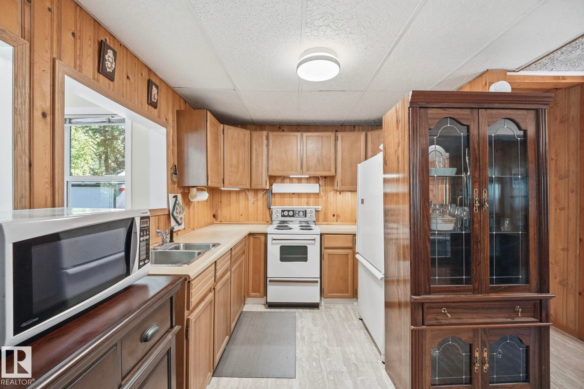 Kitchen featuring wood paneling, light wood-finish cabinetry, and light-tone countertops - 1410 47436 Range Rd. 15, Rural Leduc County, AB