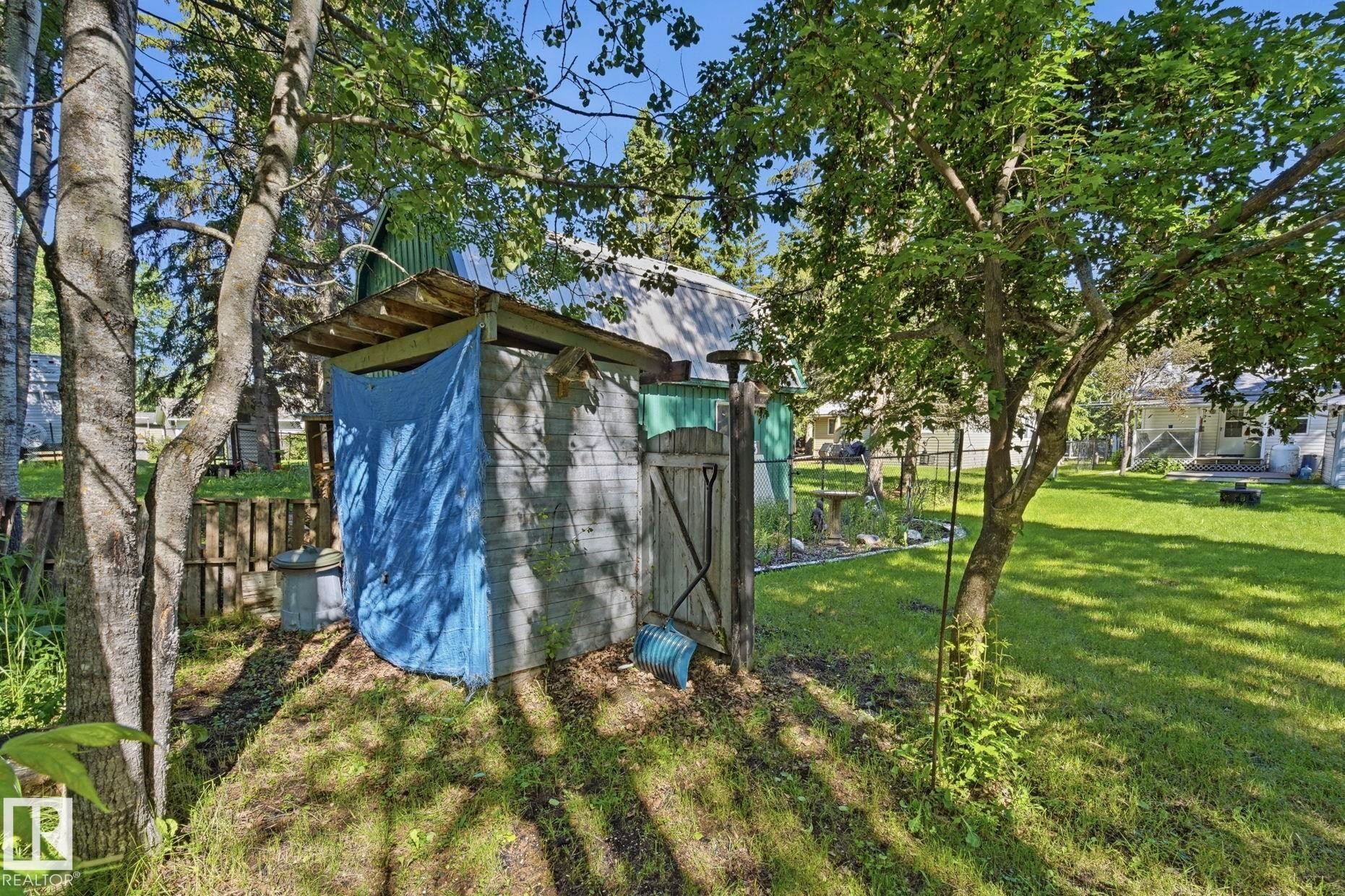 Wood-paneled shed with a metal roof and a wooden gate, situated on a grassy slope - 1410 47436 Range Rd. 15, Rural Leduc County, AB