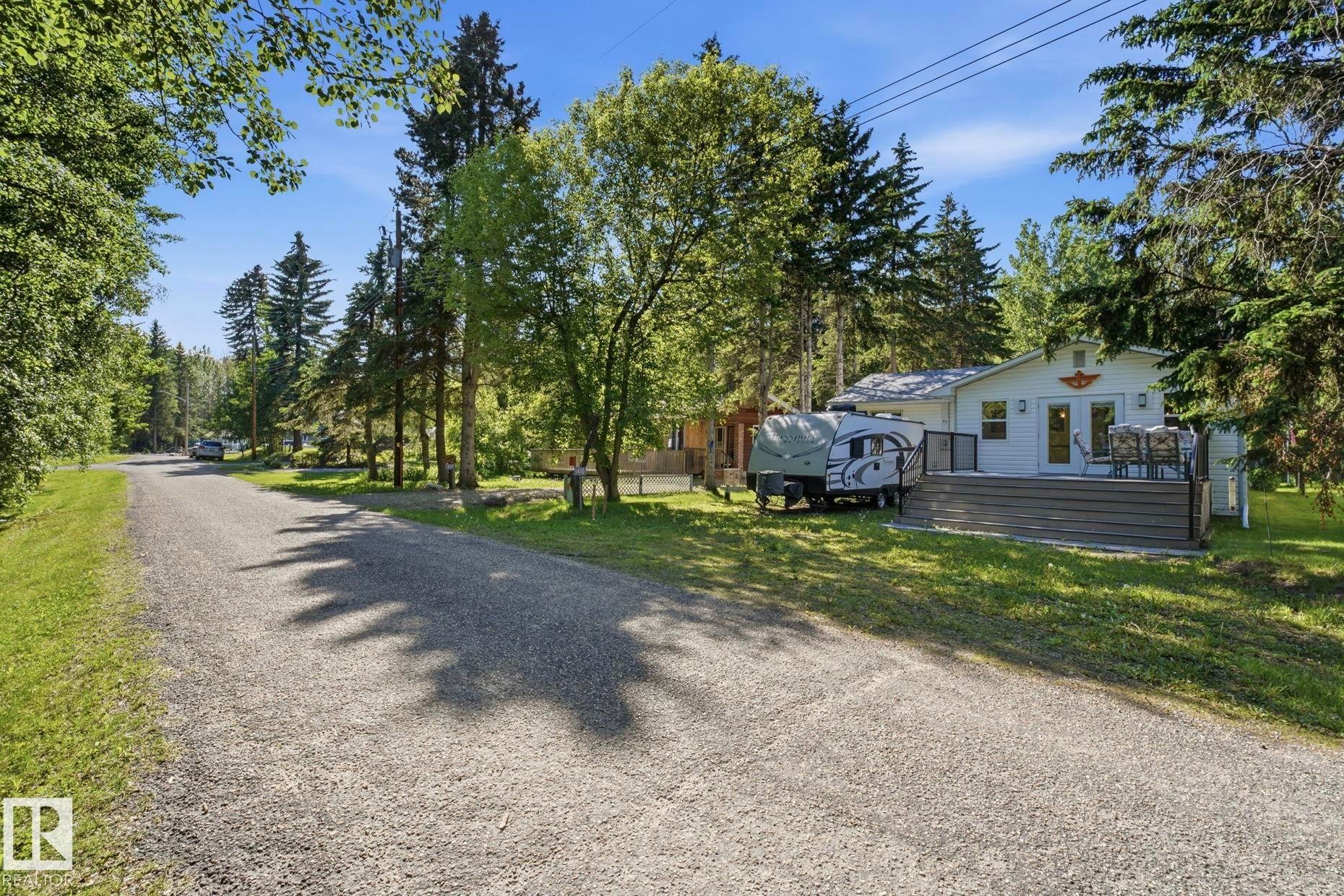 White exterior with a grey composite deck, surrounded by mature trees - 1410 47436 Range Rd. 15, Rural Leduc County, AB