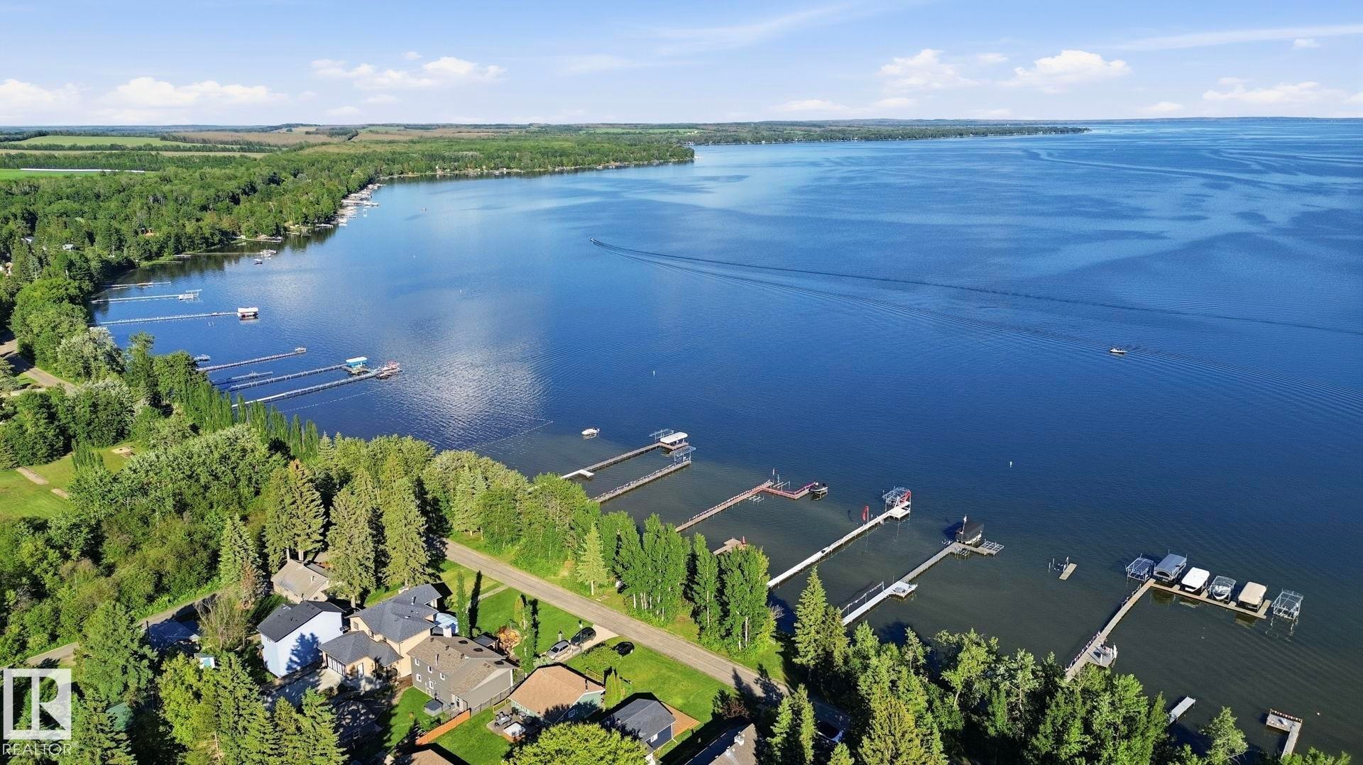 Expansive lakefront setting featuring multiple private docks and a surrounding forested landscape - 1410 47436 Range Rd. 15, Rural Leduc County, AB